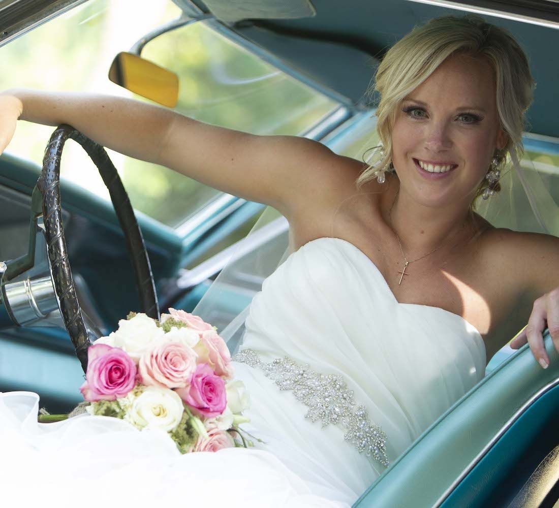 Bride holding a bouquet while seated behind the wheel of a car