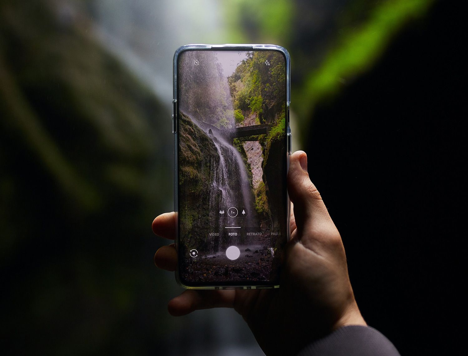 Hand holds a smartphone camera framing a waterfall