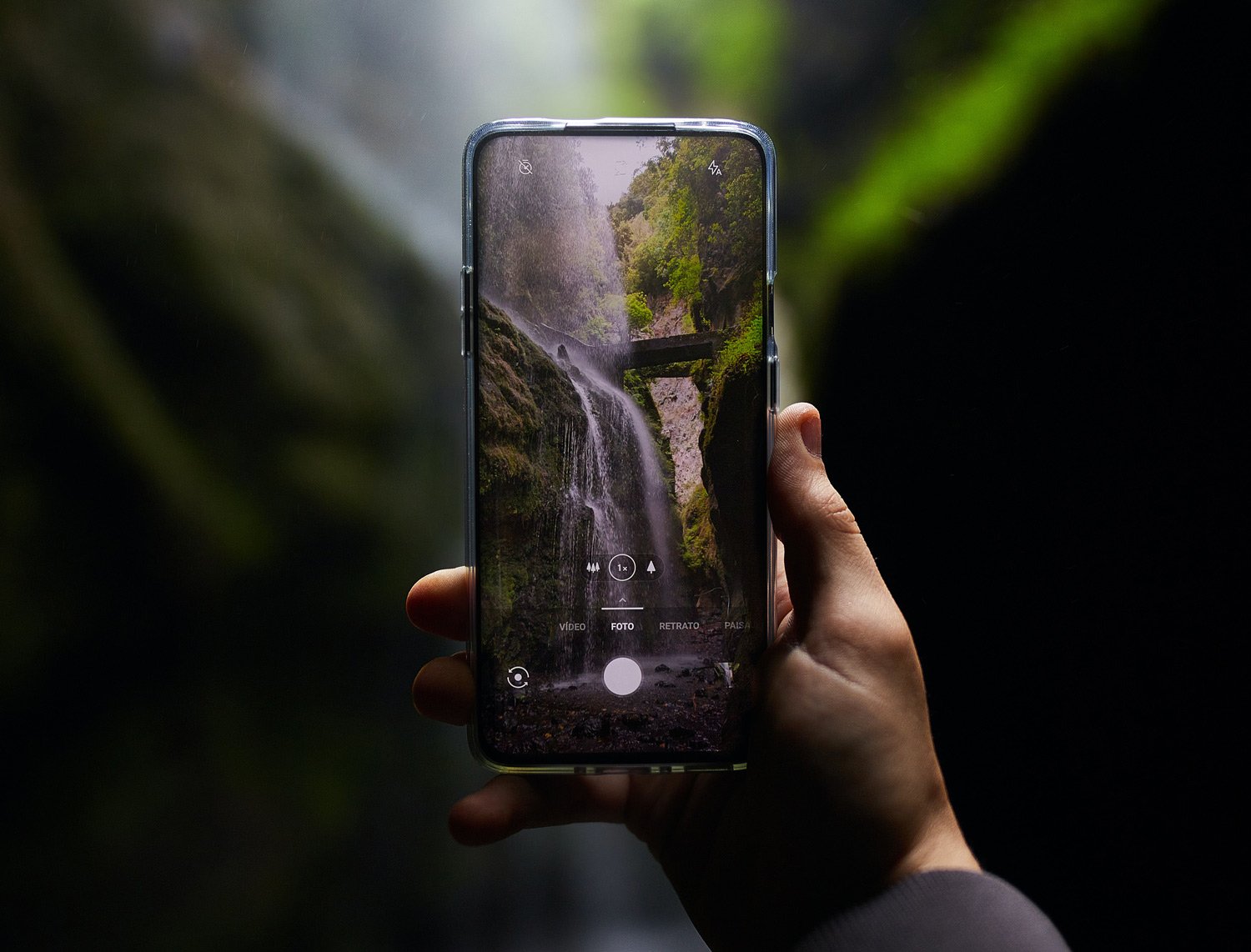 Hand holds a smartphone camera framing a waterfall