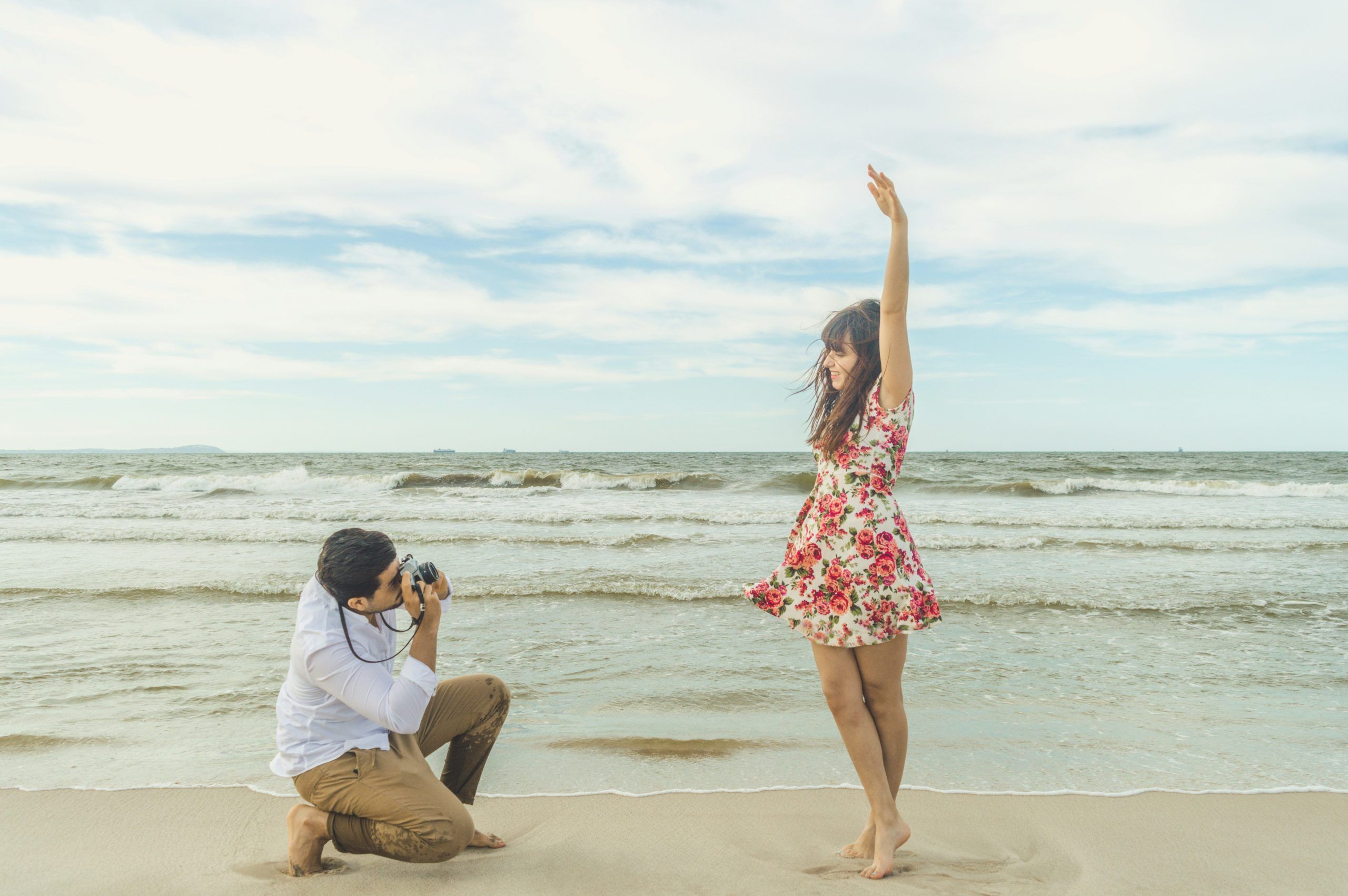 Photographer kneels to photograph a woman posing on the beach