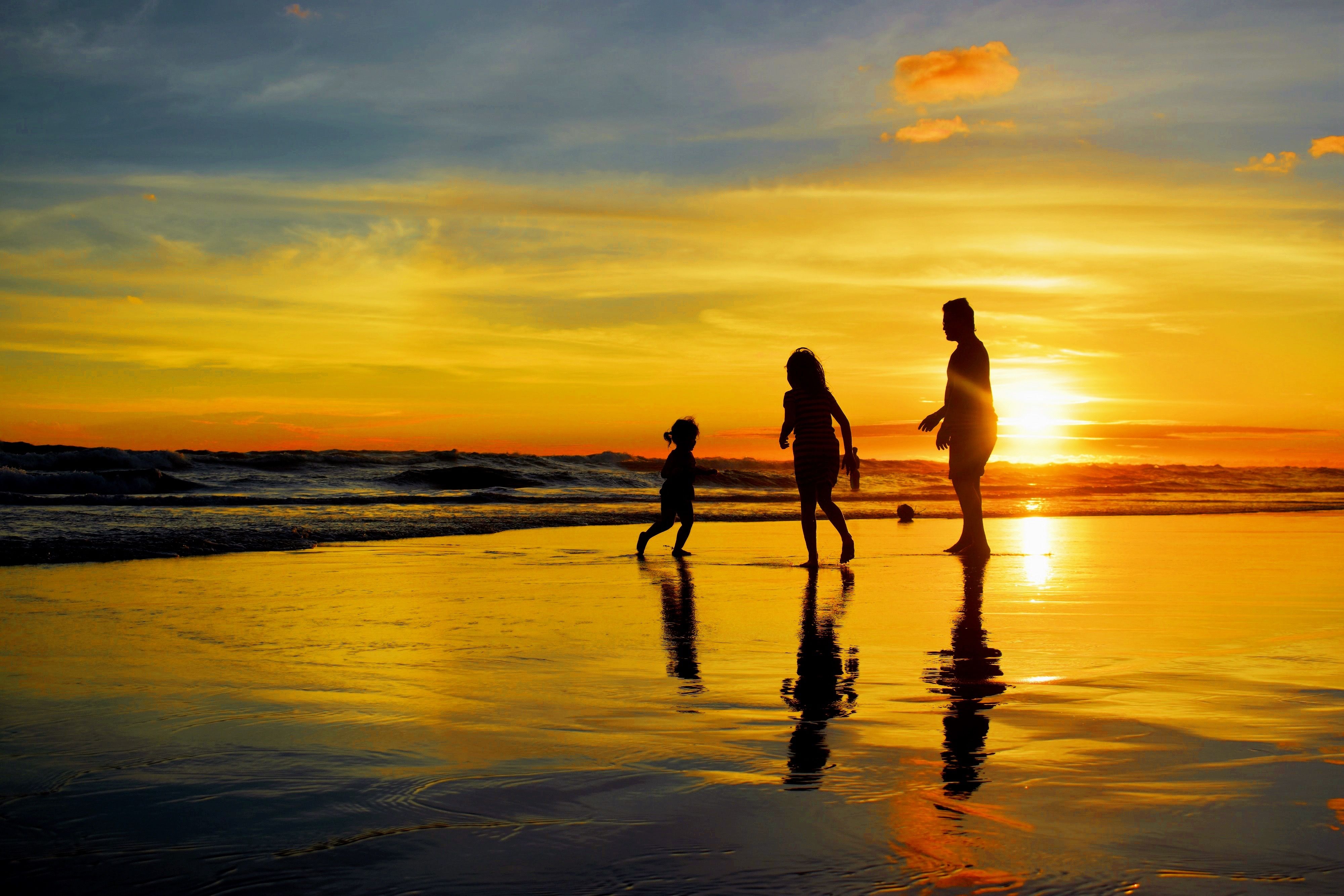 Family plays at the ocean's edge during sunset
