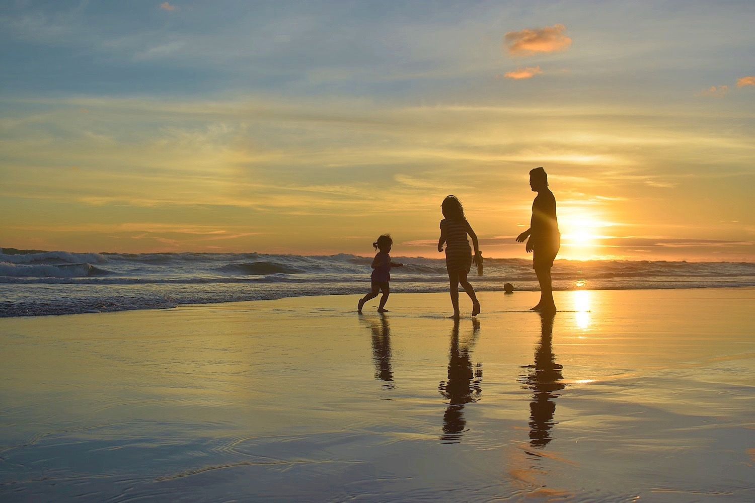 Adult and two children walk along the beach at sunset