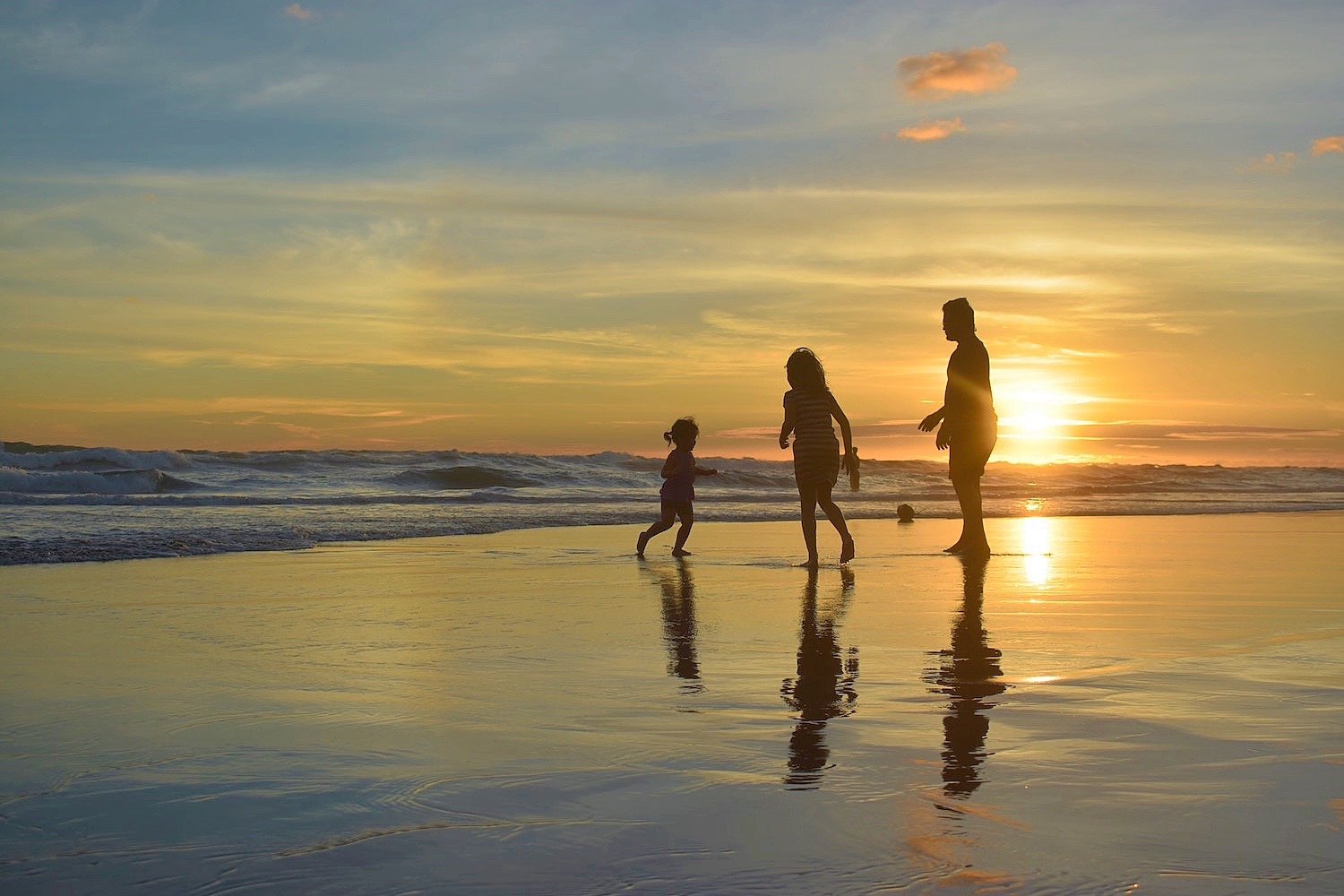 Adult and two children walk along the beach at sunset