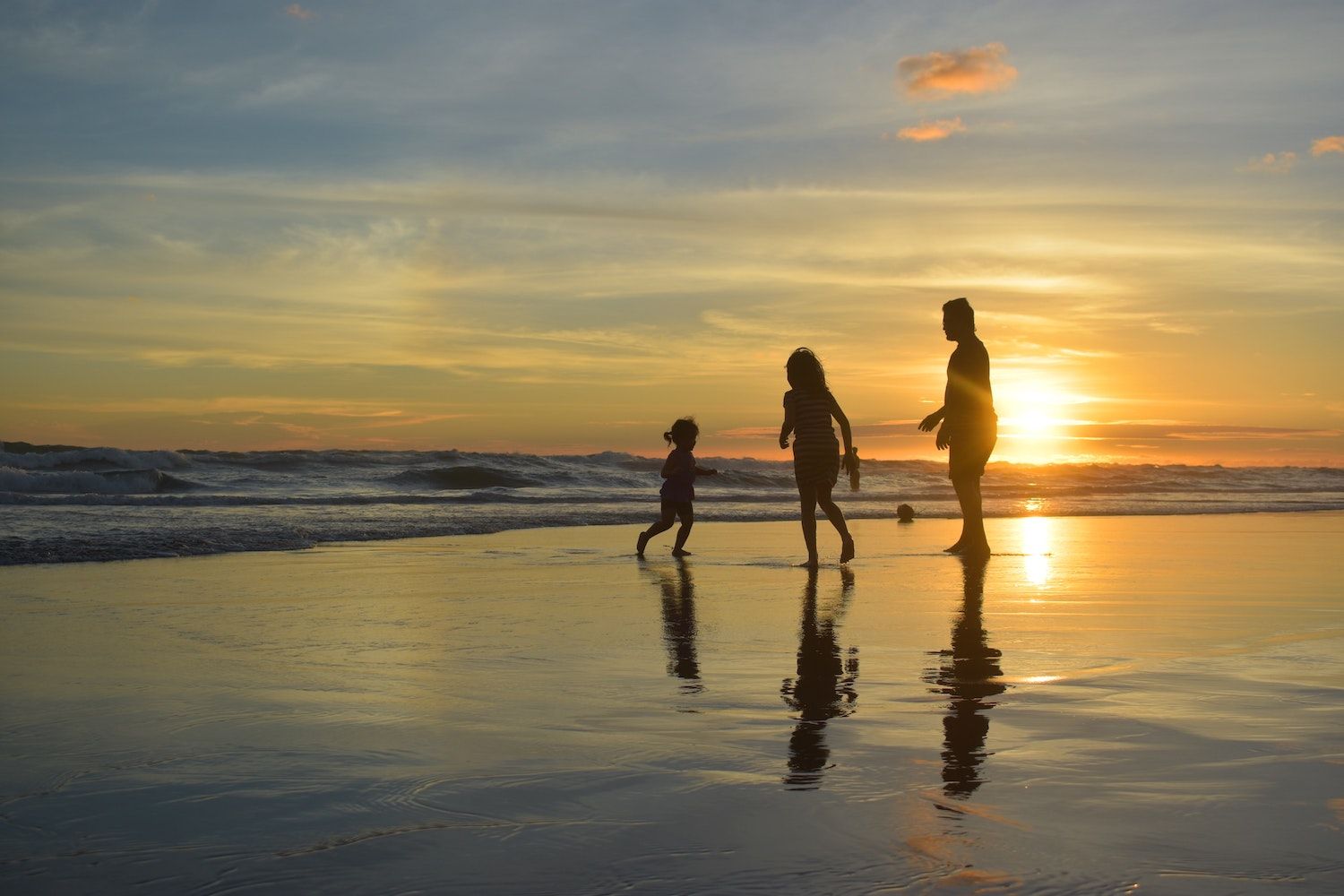 Adult and two children play at the shoreline during sunset