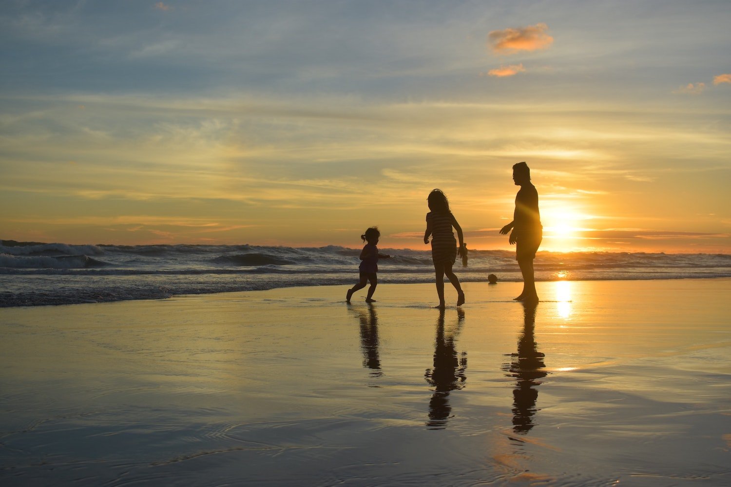 Adult and two children play at the shoreline during sunset