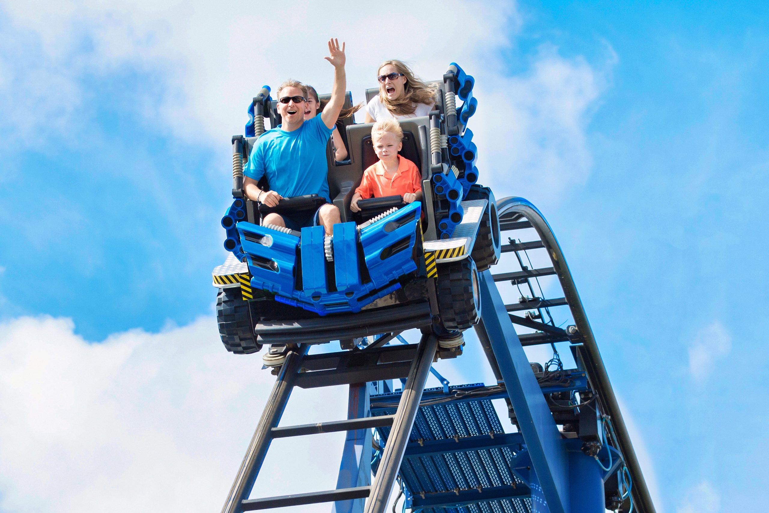 Family rides a roller coaster as two adults raise their hands