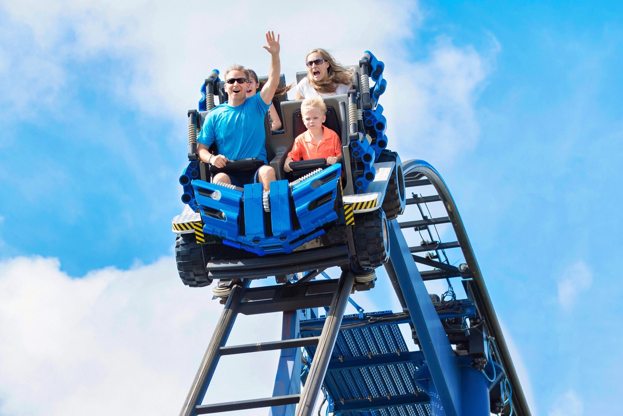 Family rides a roller coaster as two adults raise their hands