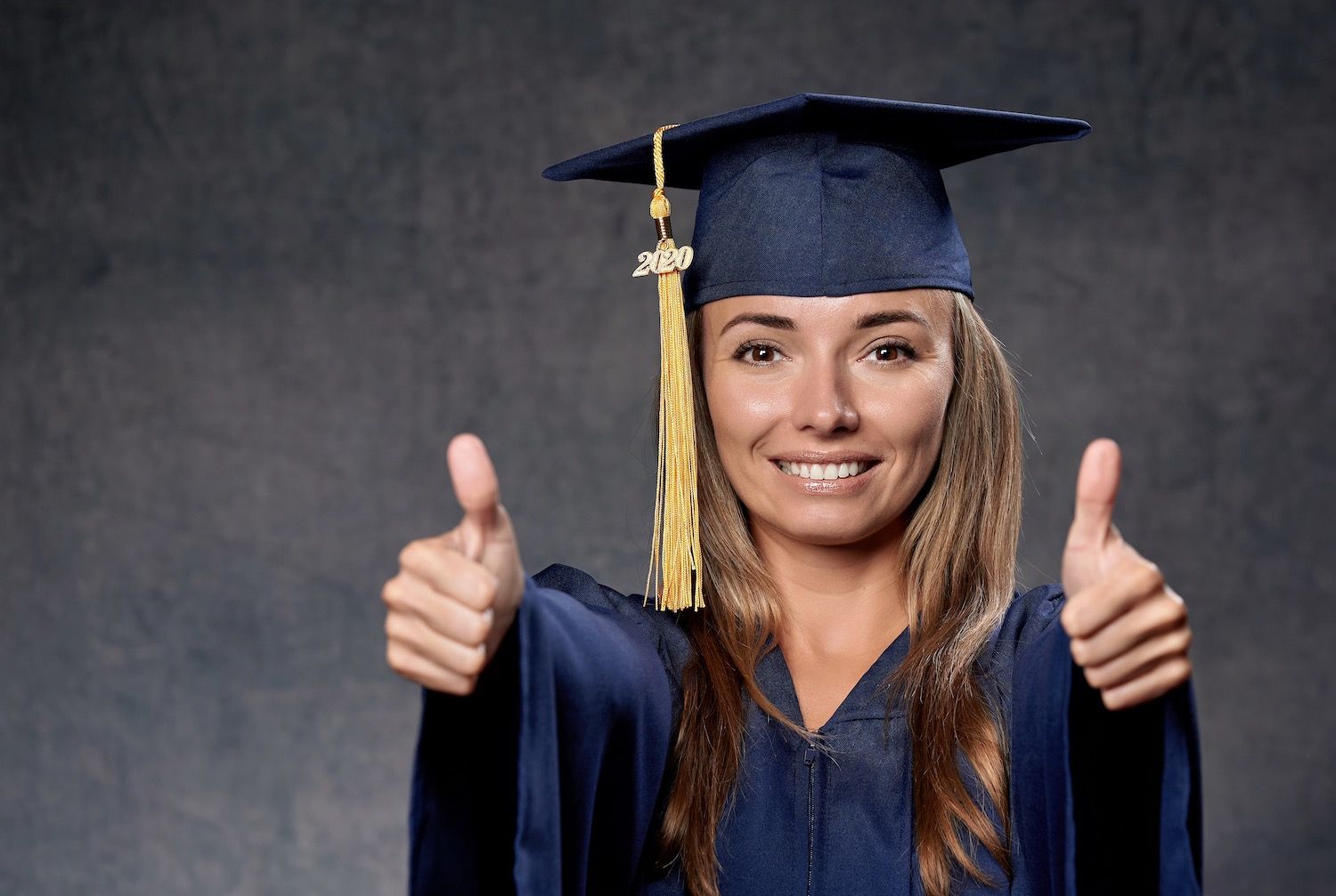 Graduate in cap and gown gives two thumbs up