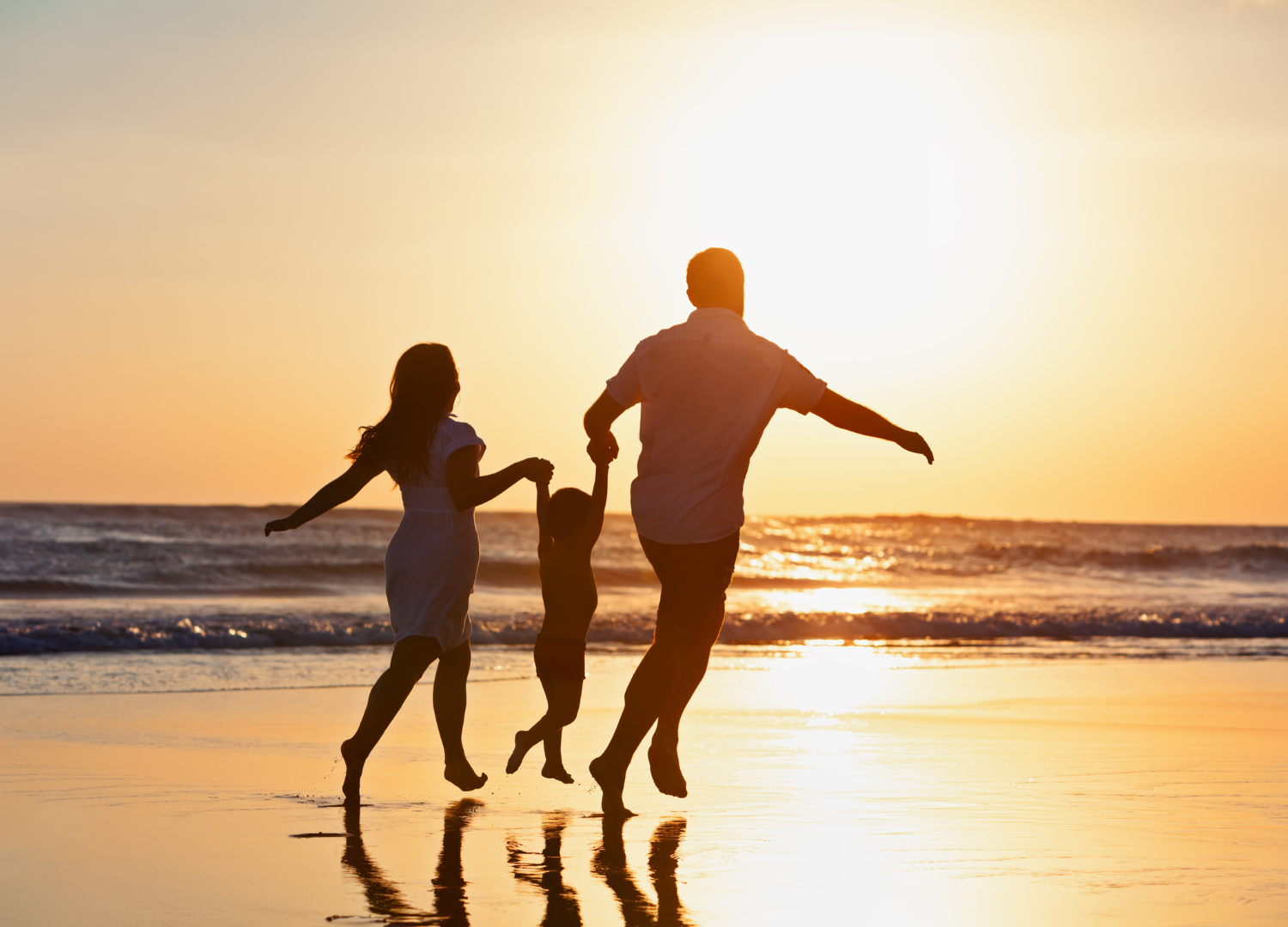 Family holding hands and jumping on a beach at sunset