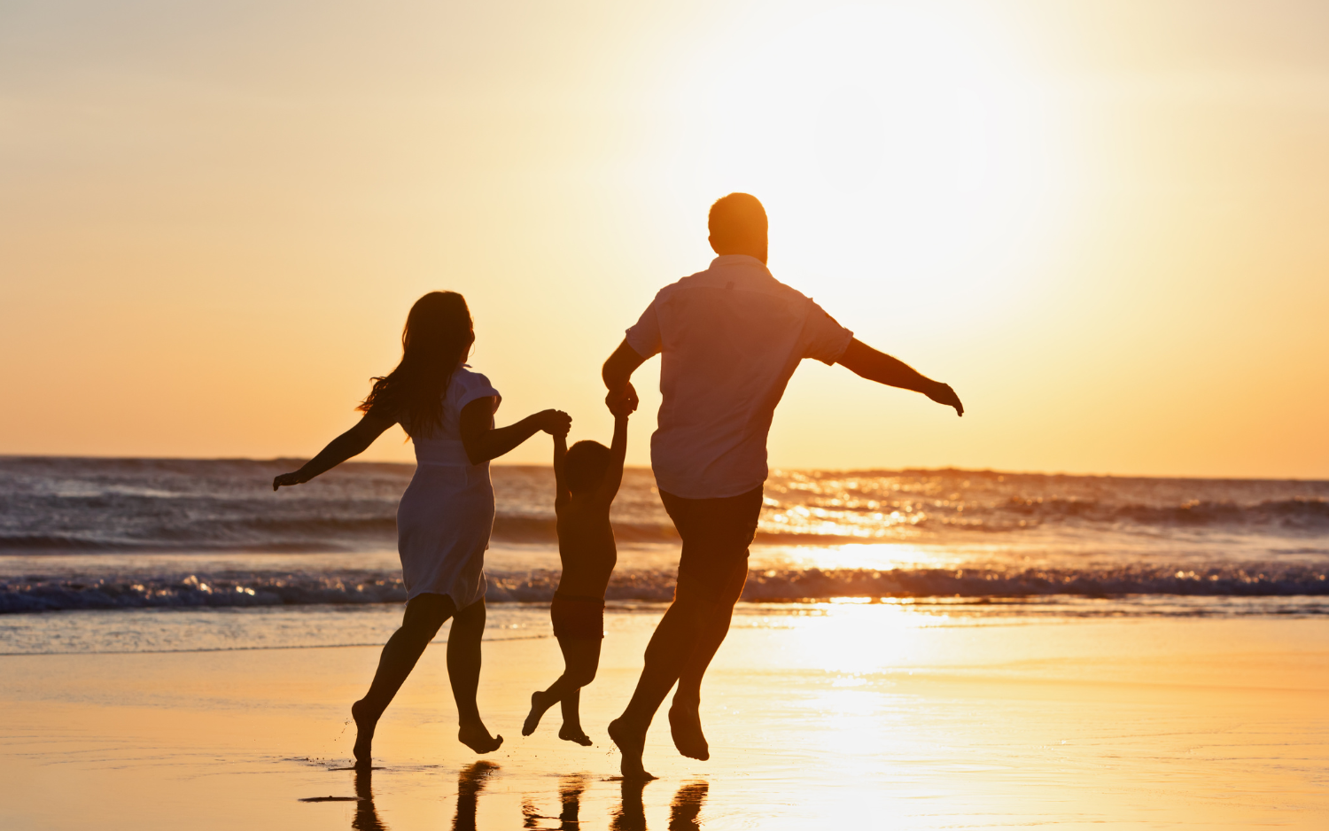 Family holding hands and jumping on a beach at sunset