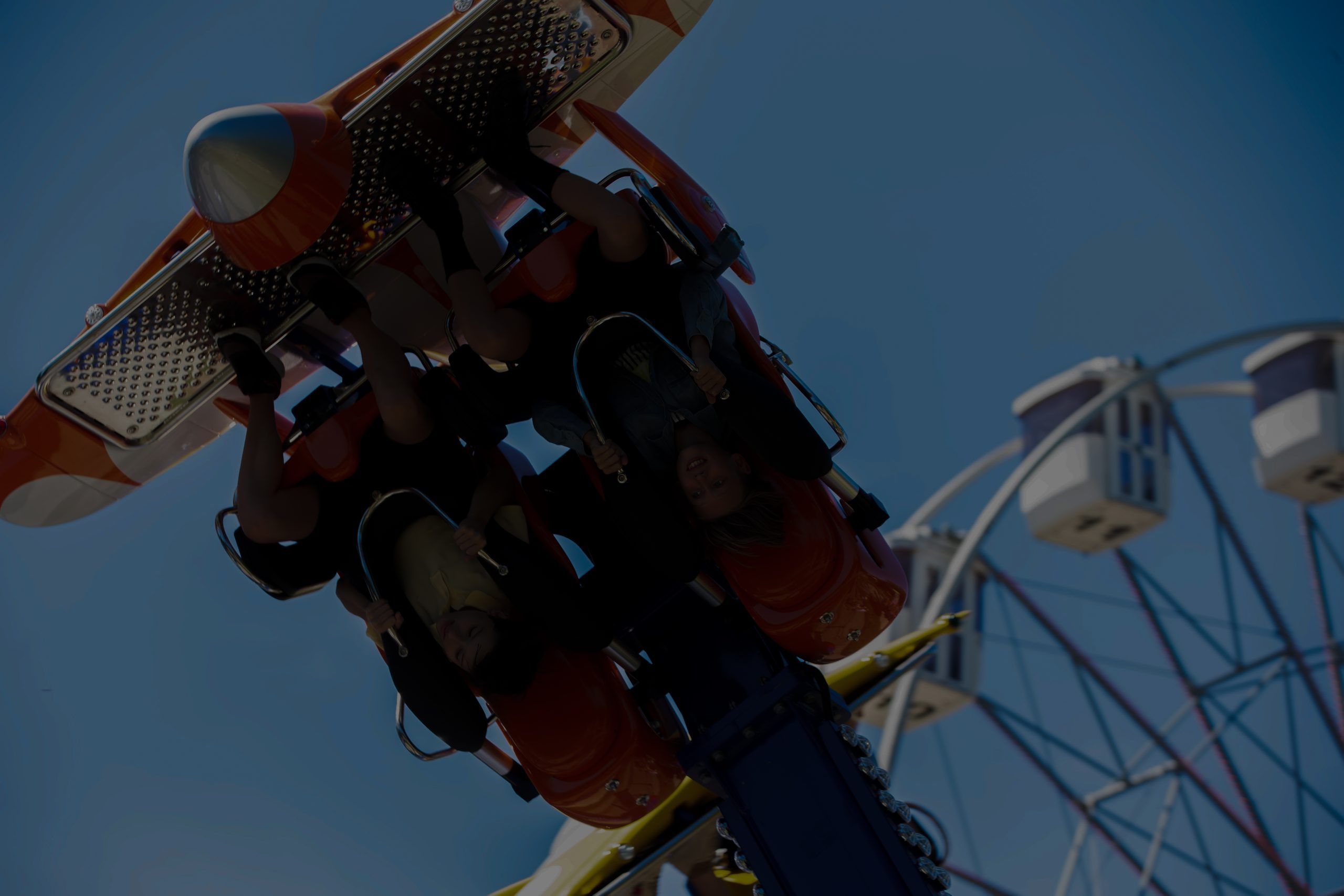 Riders hang upside down on an amusement ride near a Ferris wheel
