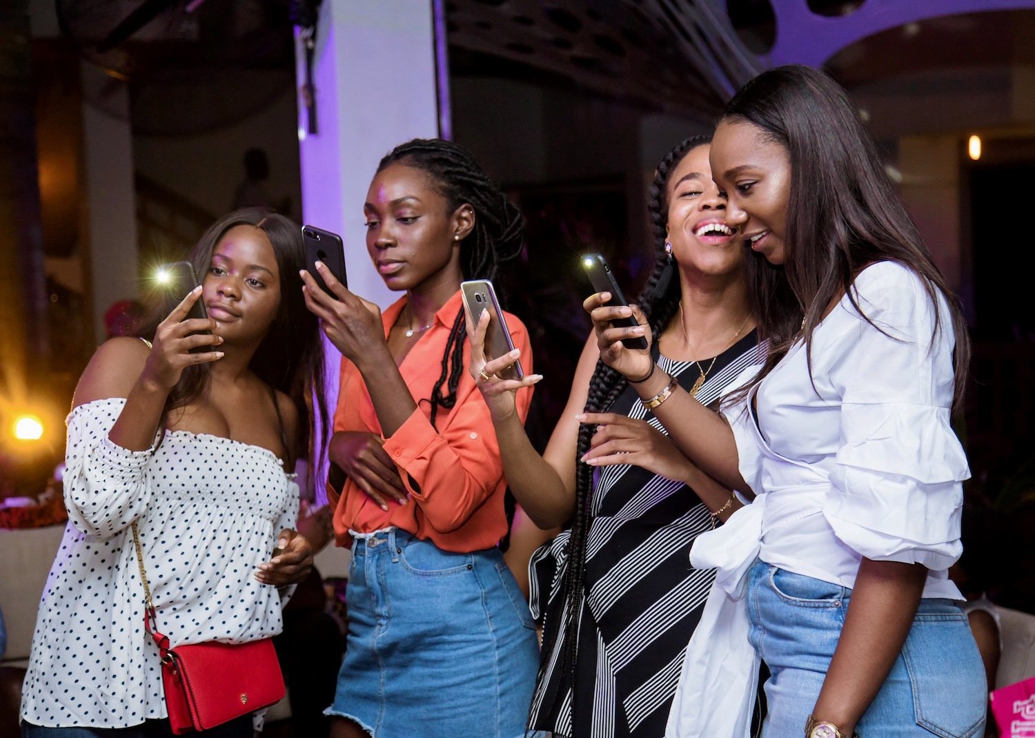 Four women look at their phones during a nighttime gathering