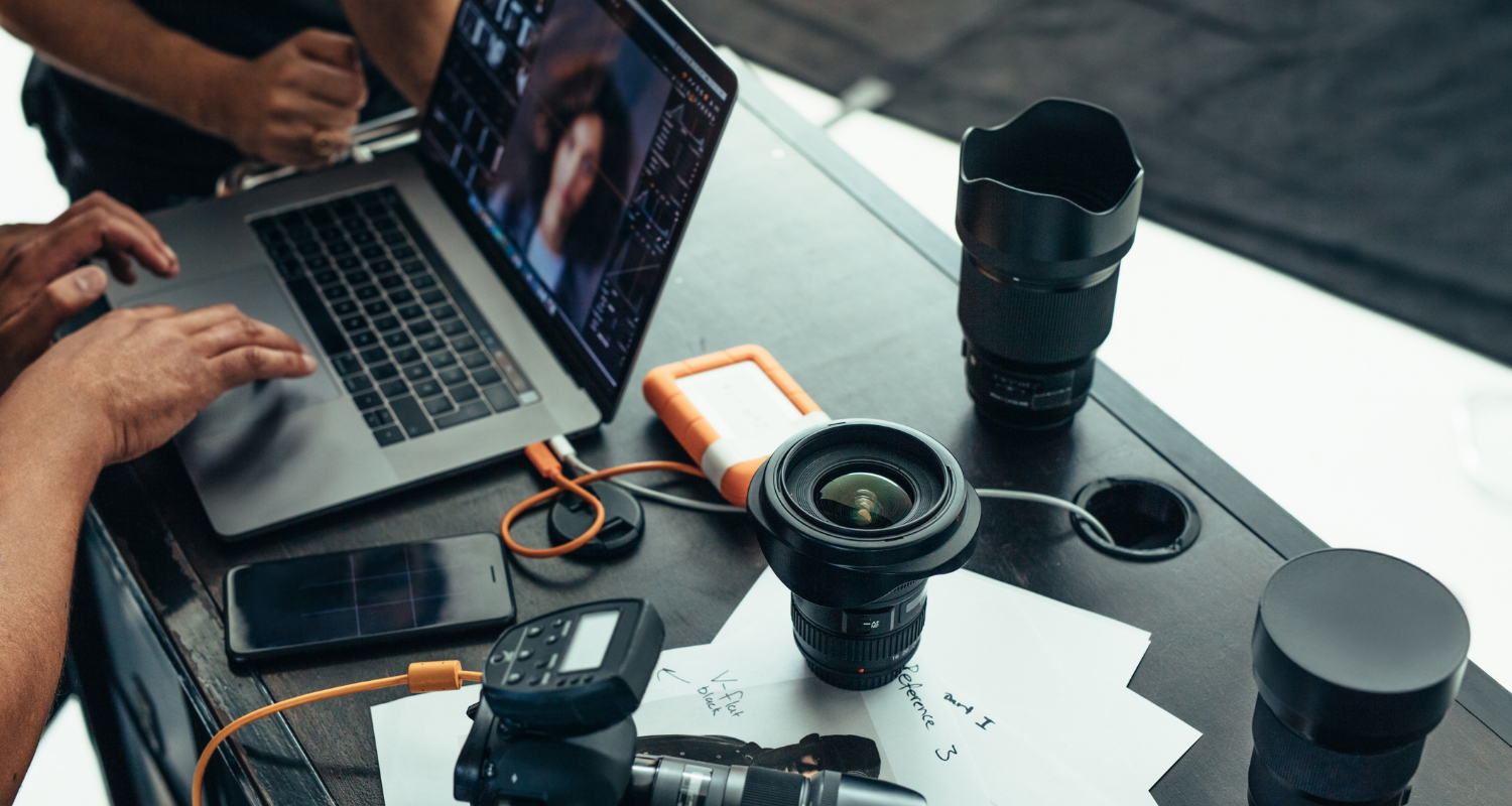 Photographers review images on a laptop beside cameras and lenses