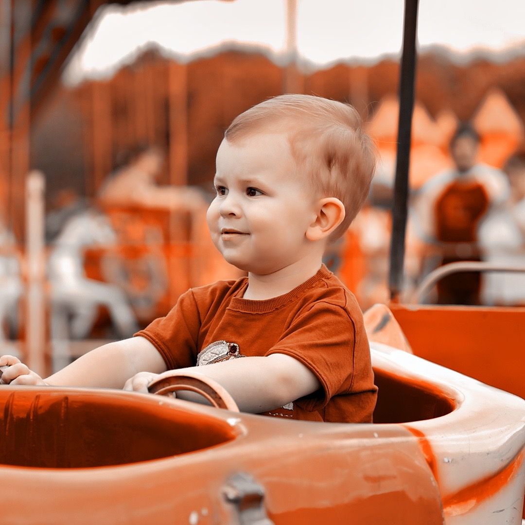 Young child holds the steering wheel of an amusement park ride