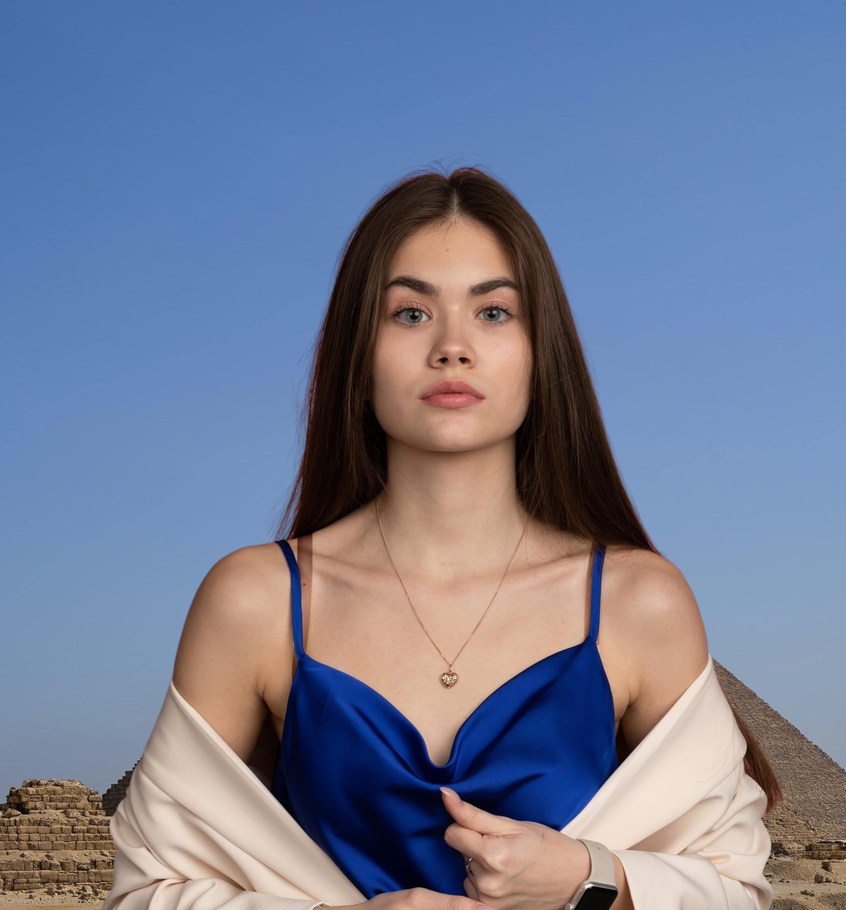 Woman in blue dress and shawl poses before pyramids