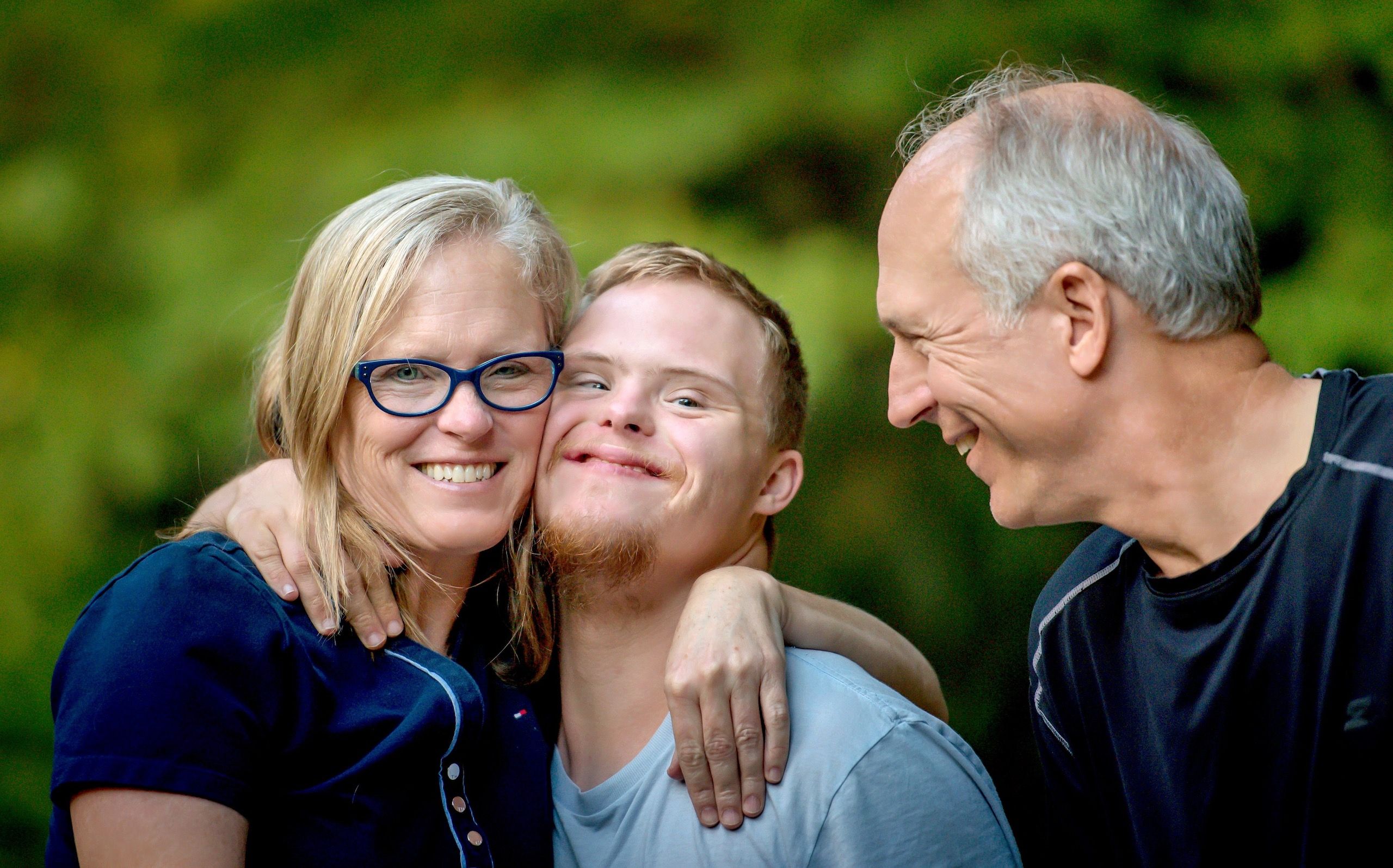 Three family members embrace and smile together outdoors