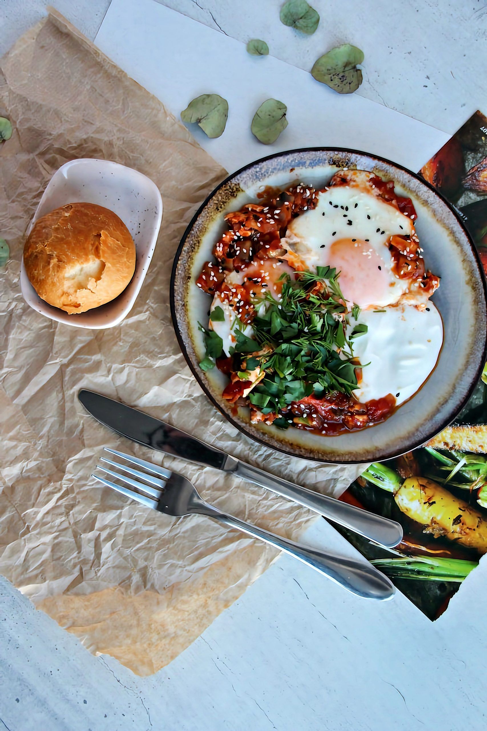Fried eggs with tomato sauce, sesame seeds, herbs and bread roll