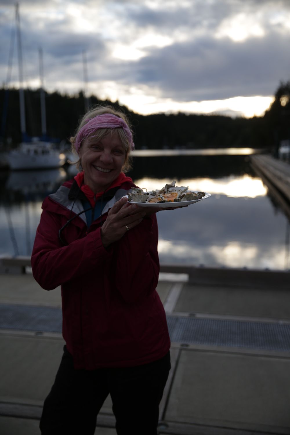 Woman holds a plate of oysters beside a marina