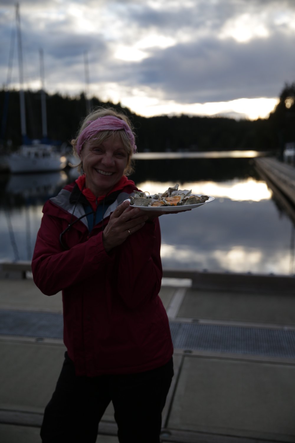 Woman holds a plate of oysters beside a marina