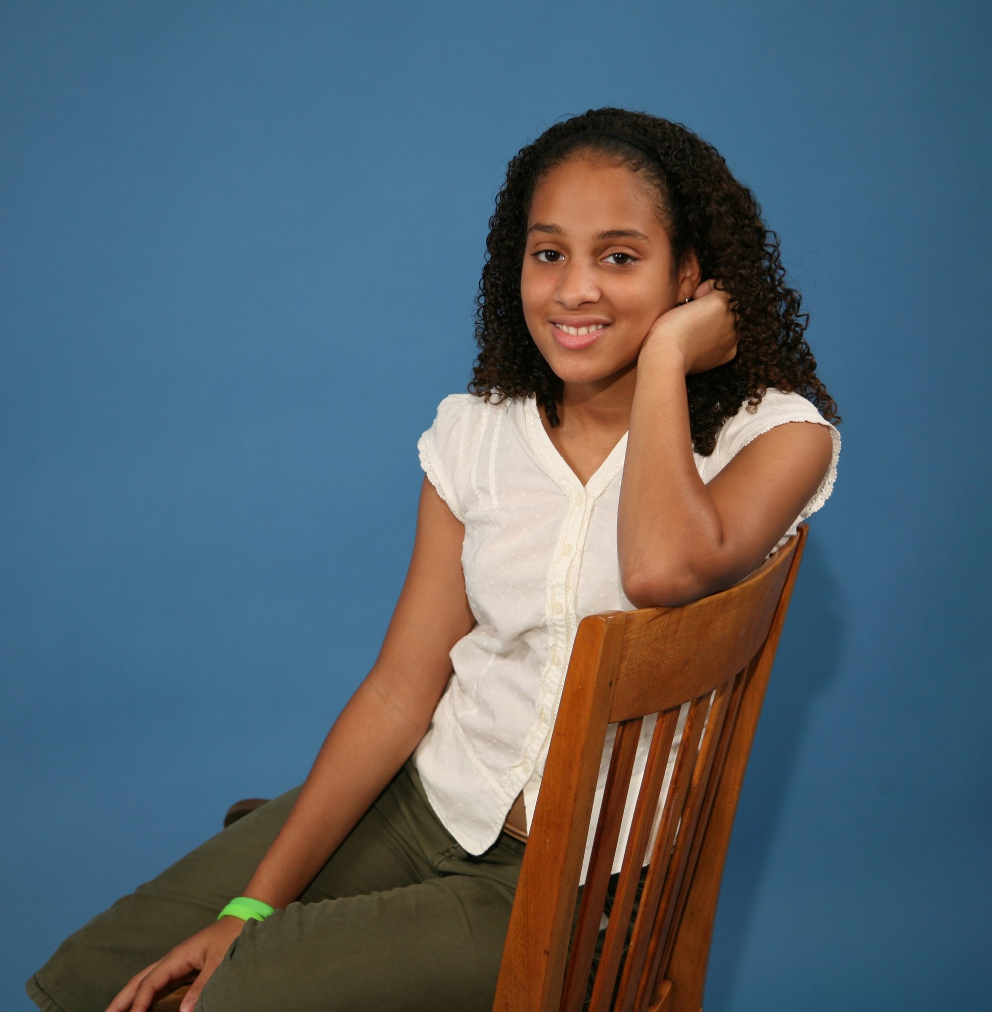 Smiling girl leaning on a wooden chair in a studio portrait