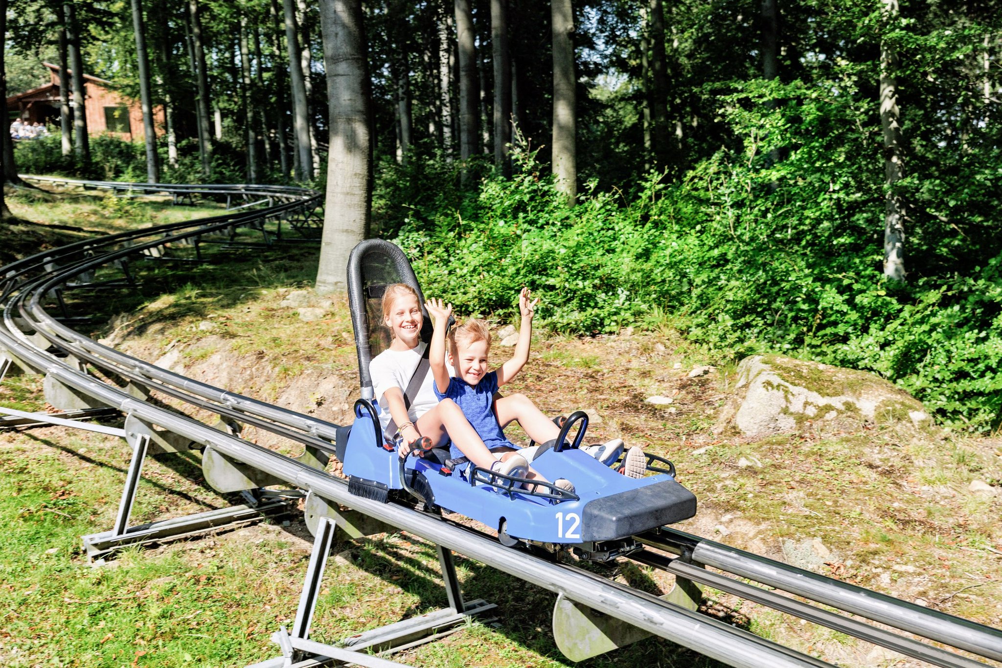 Woman and boy riding a forest alpine coaster, an overexposed photo after correction