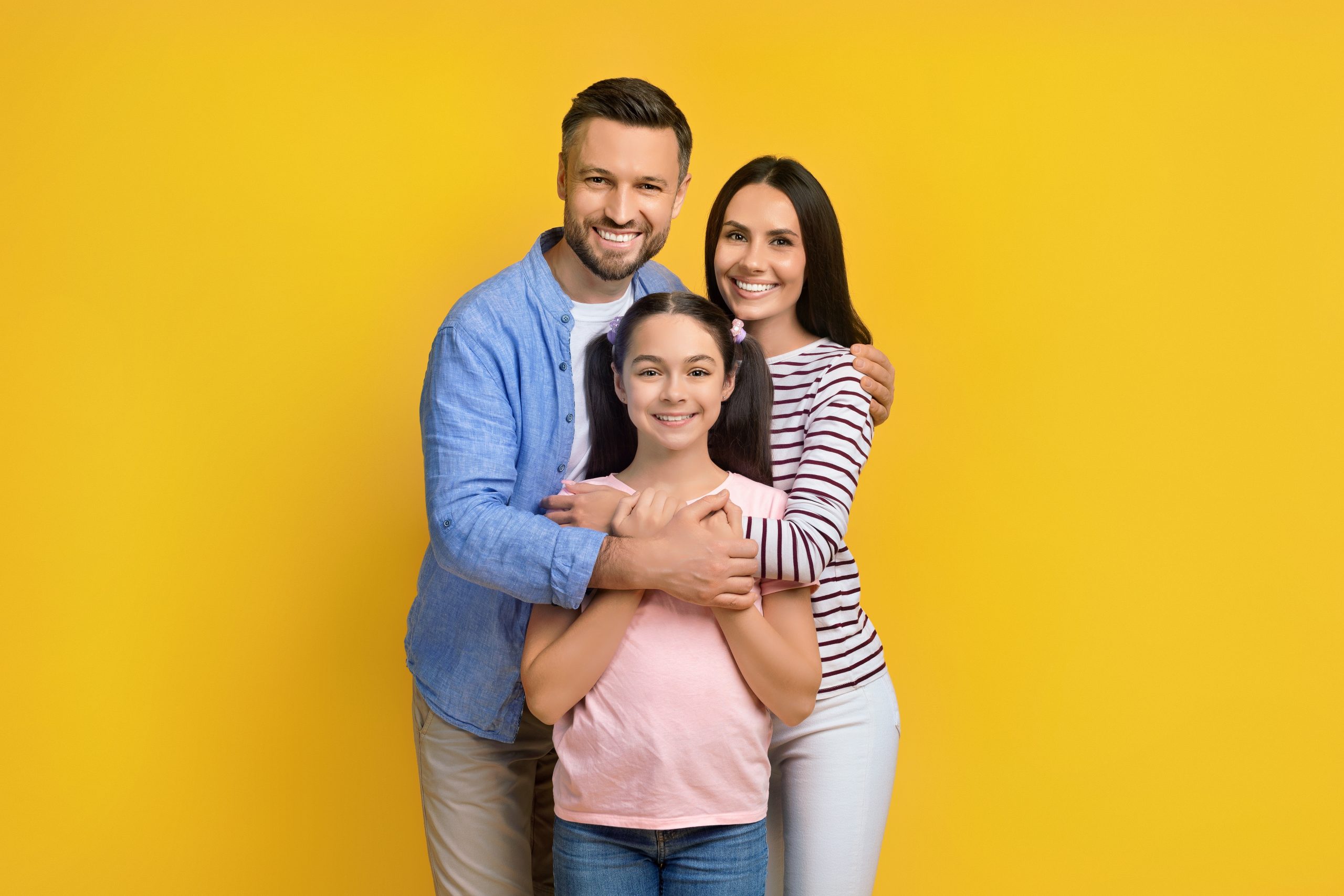 Smiling family of three posing together against a yellow backdrop