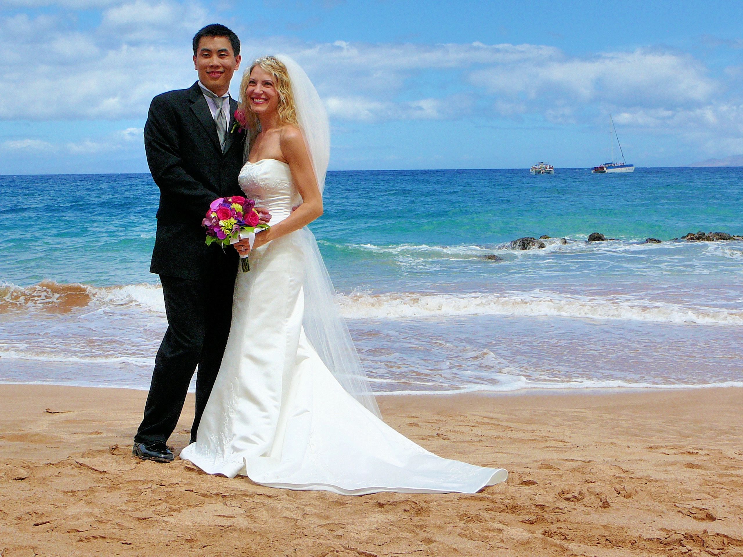 Bride and groom posing on a beach with the sea behind them
