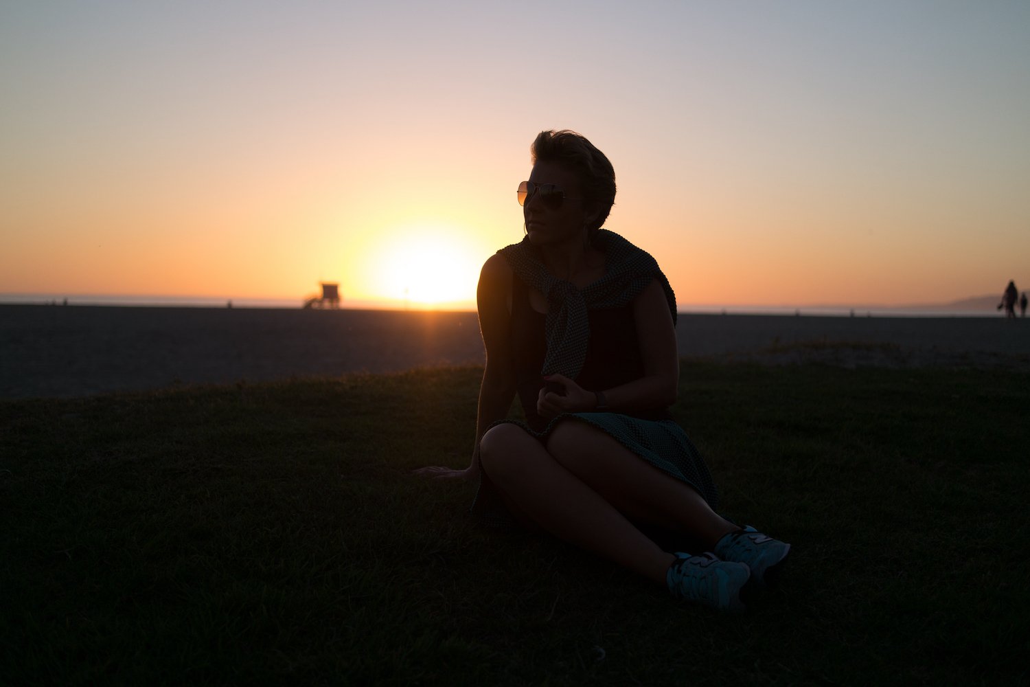 Backlit woman sitting on grass at sunset, her face in shadow