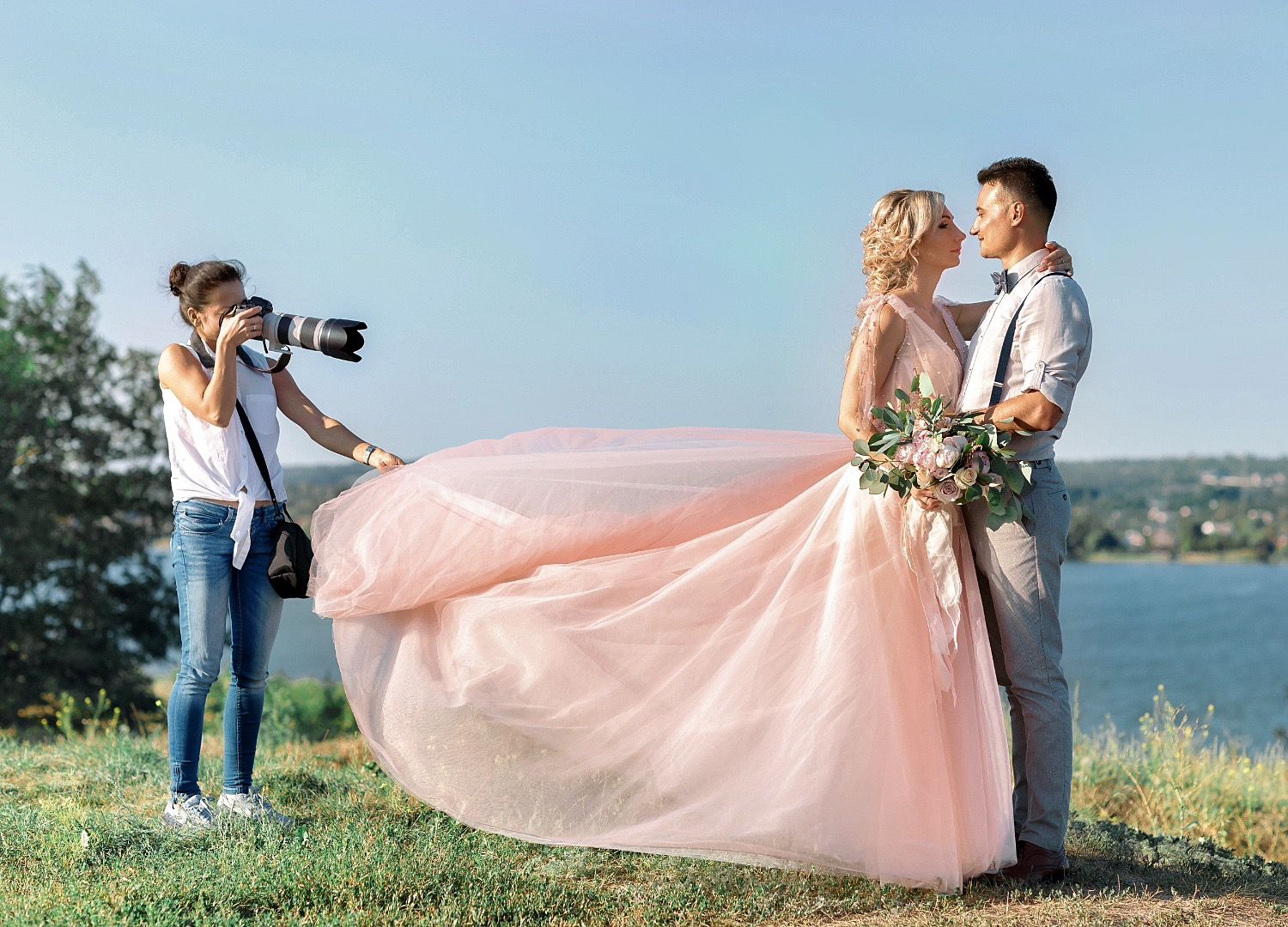 Photographer shooting a bride and groom as her pink gown blows in the wind
