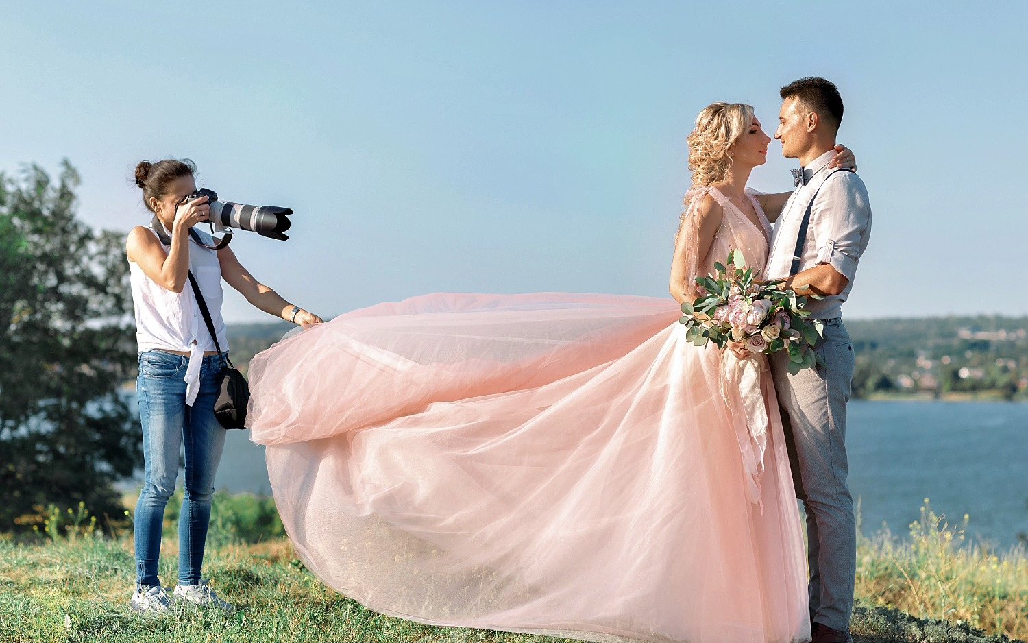 Photographer shooting a bride and groom as her pink gown blows in the wind