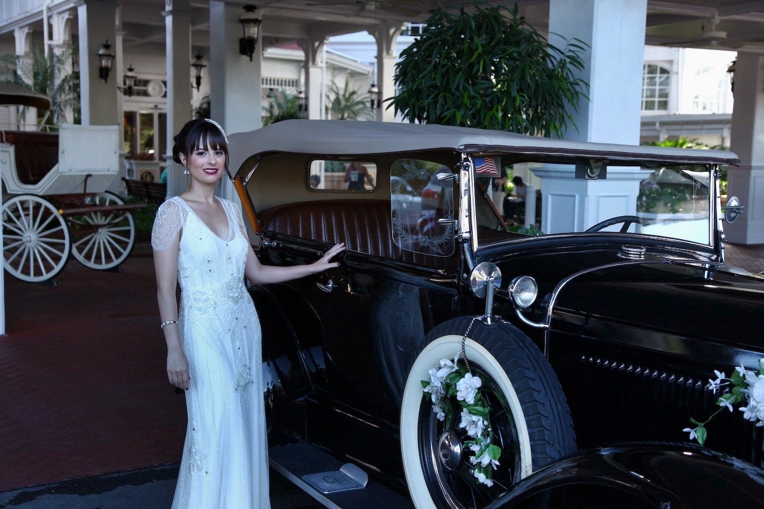 Bride standing beside a vintage black car decorated with flowers
