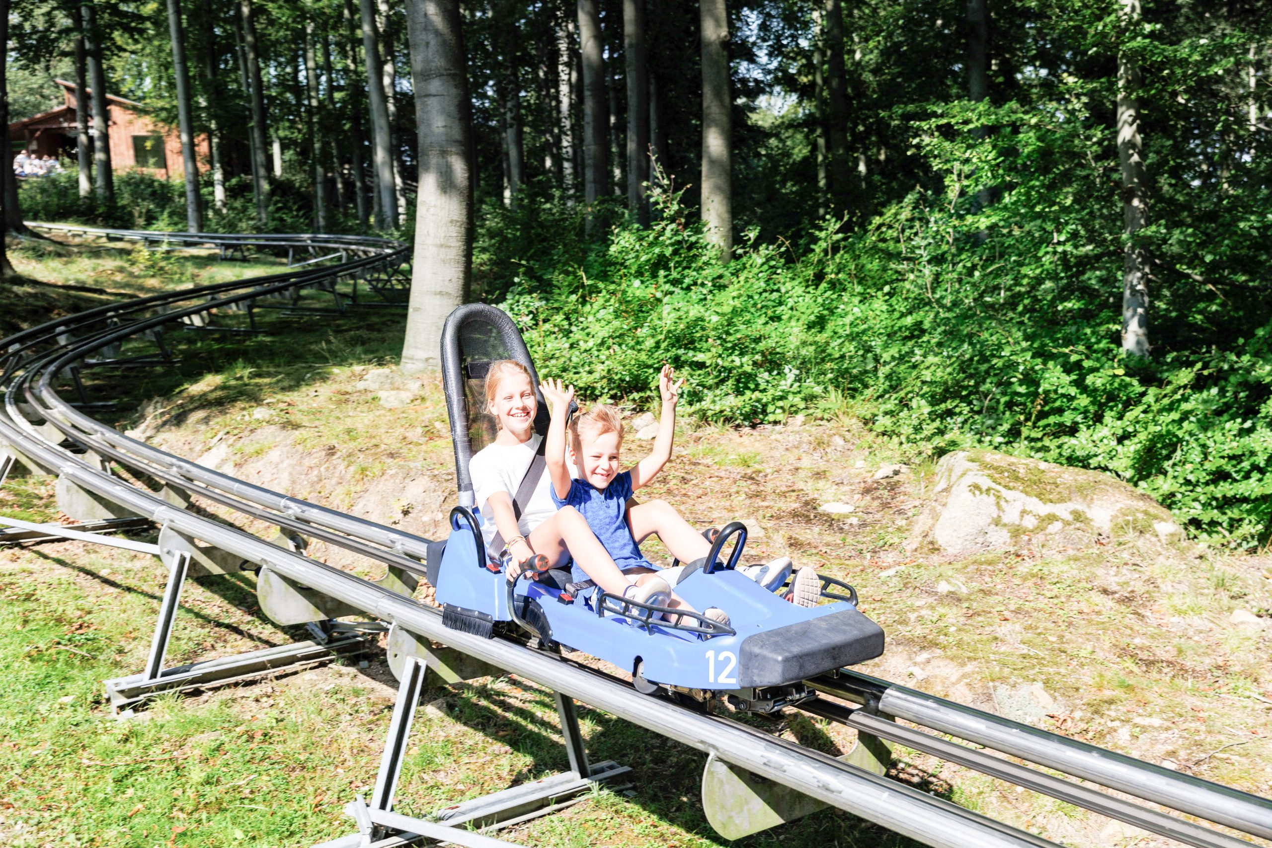 Woman and child waving on a forest alpine coaster, overexposed