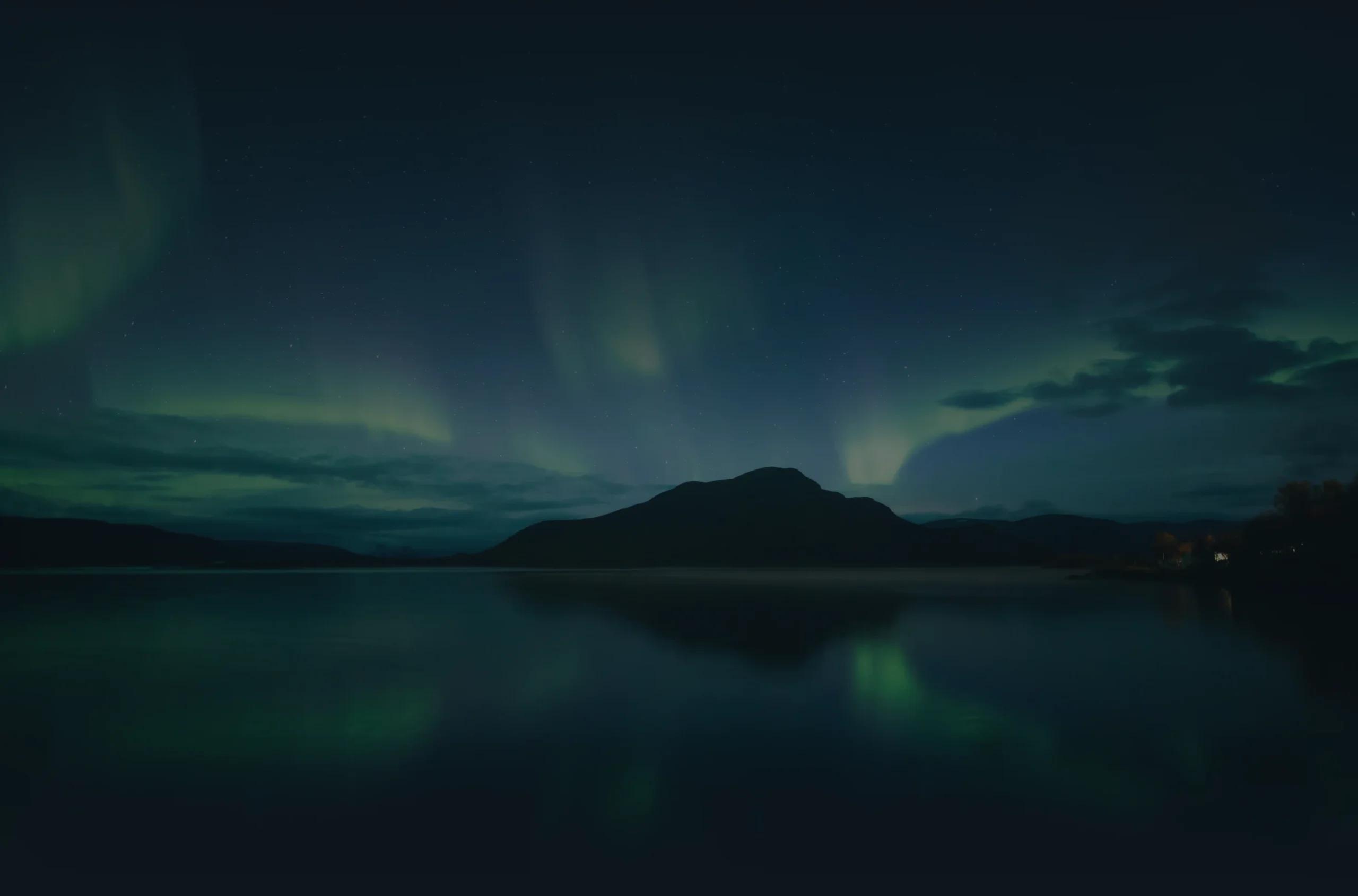Northern lights over a mountain reflected in a lake at night