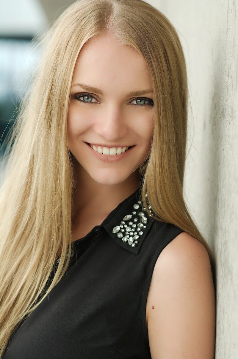Portrait of a smiling young woman with long blonde hair leaning against a wall