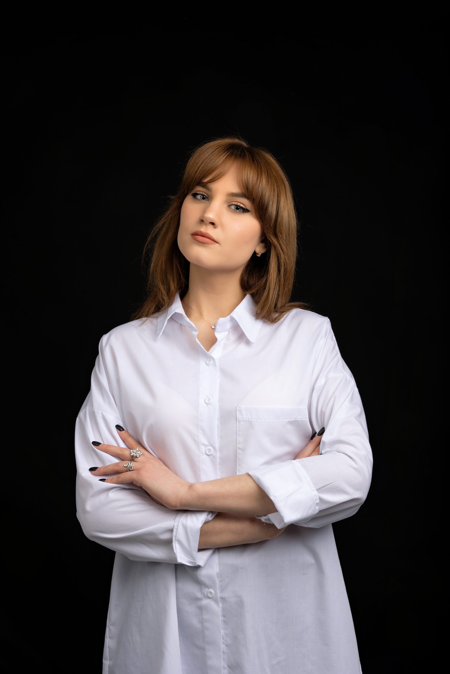 Portrait of a woman in a white shirt with arms crossed against a black background