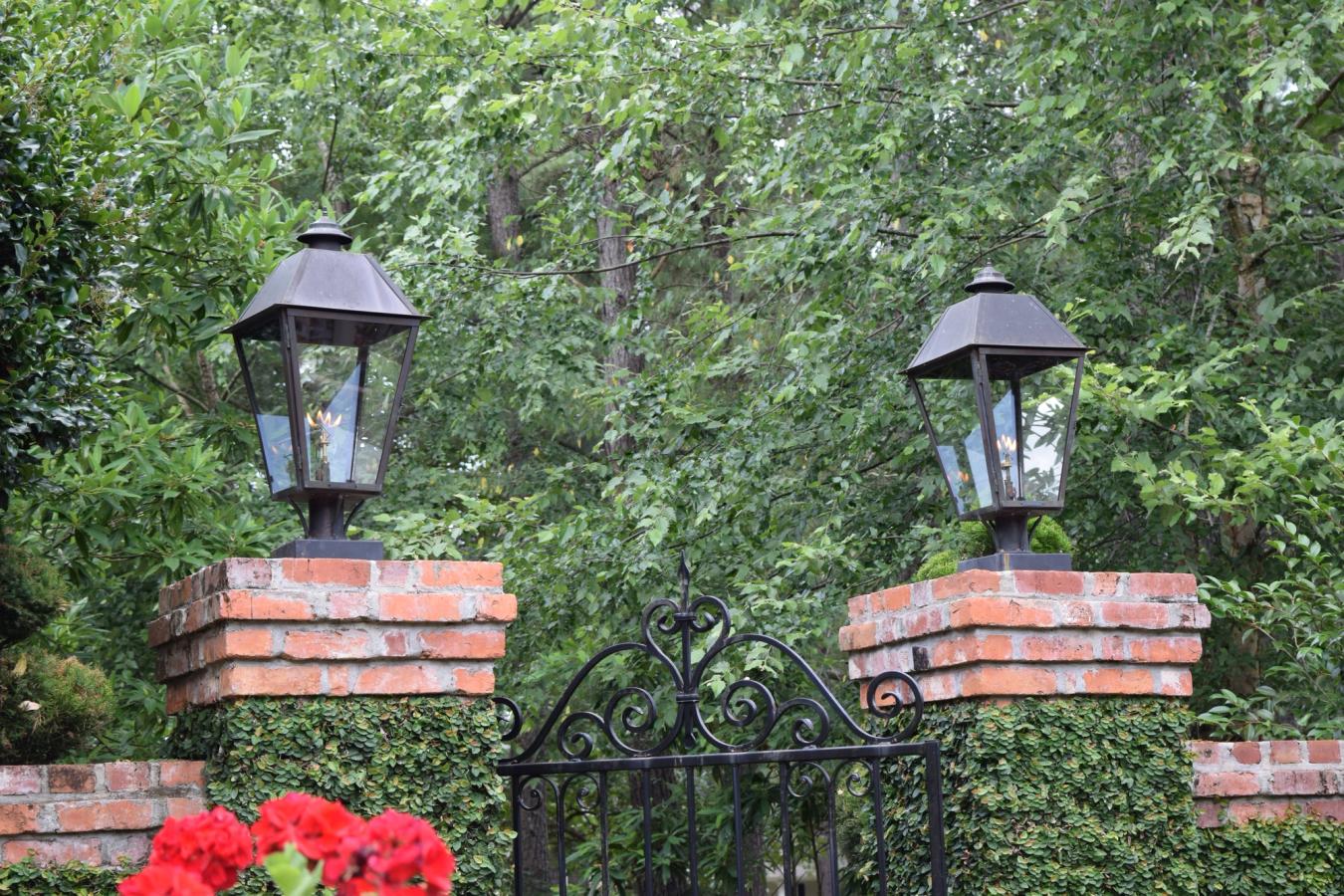Gas lanterns mounted on brick driveway piers flanking an iron entry gate