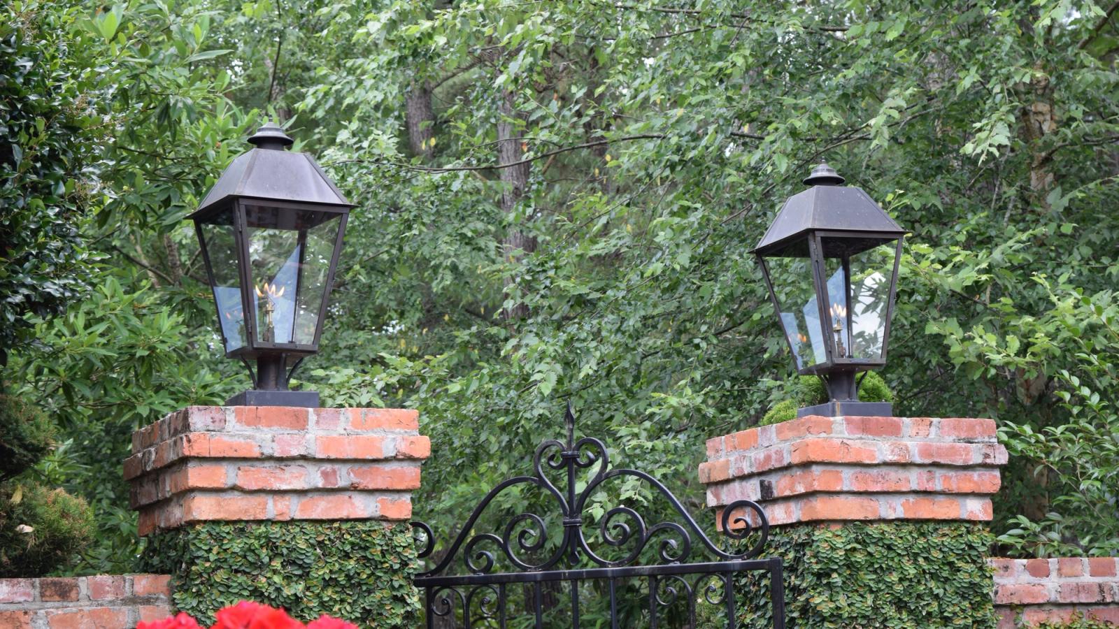 Gas lanterns mounted on brick driveway piers flanking an iron entry gate