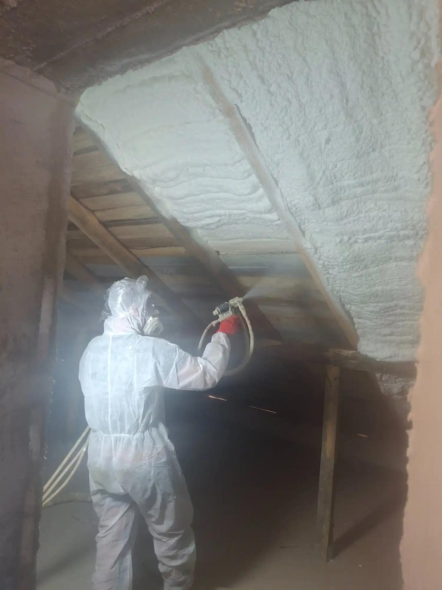 Aplicator profesionist în echipament de protecție pulverizând spumă poliuretanică cu celulă deschisă pe astereala podului – Termoizolații România, Horezu, Vâlcea