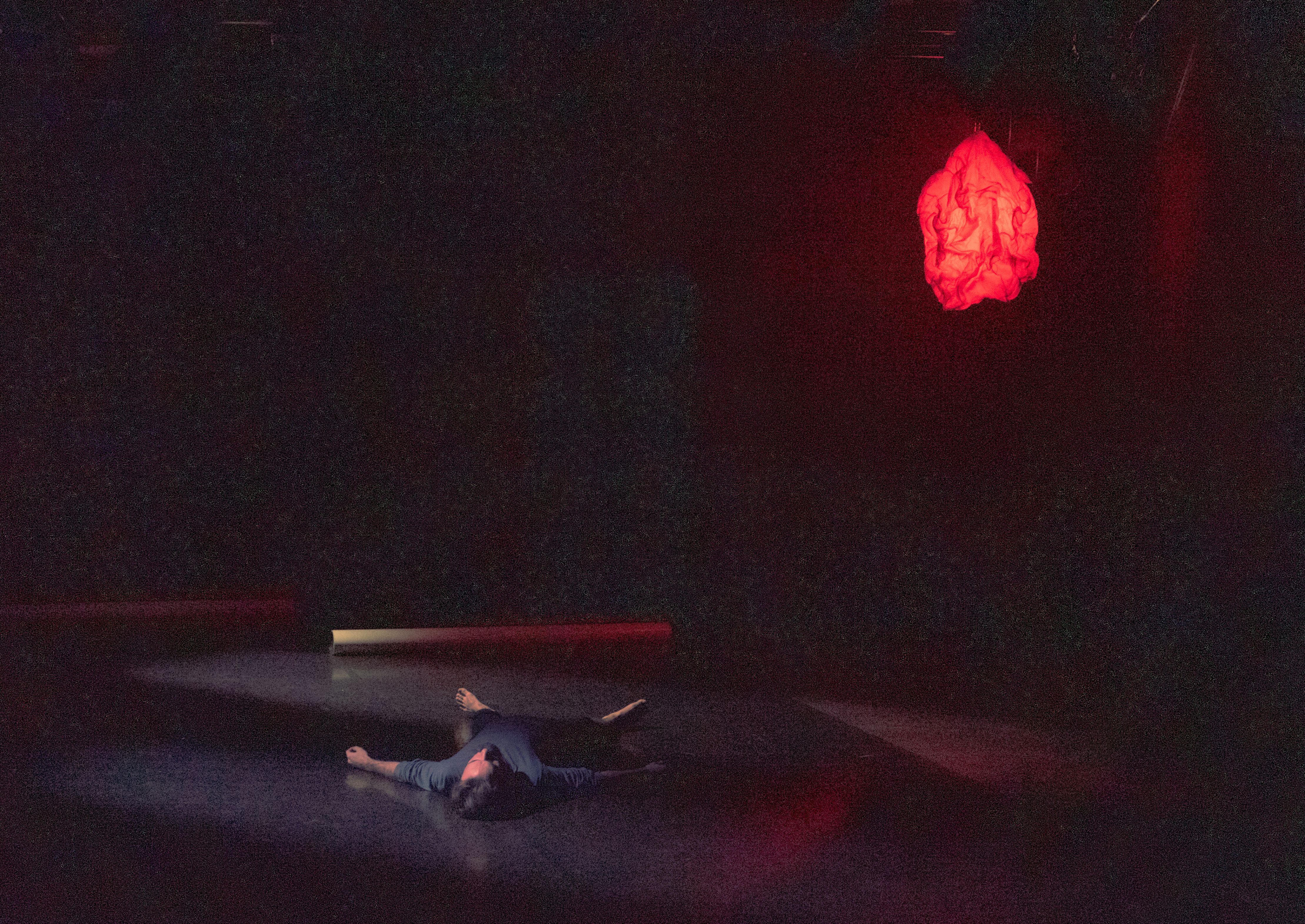 mężczyzna leżący na scenie w świetle czerwonej lampy