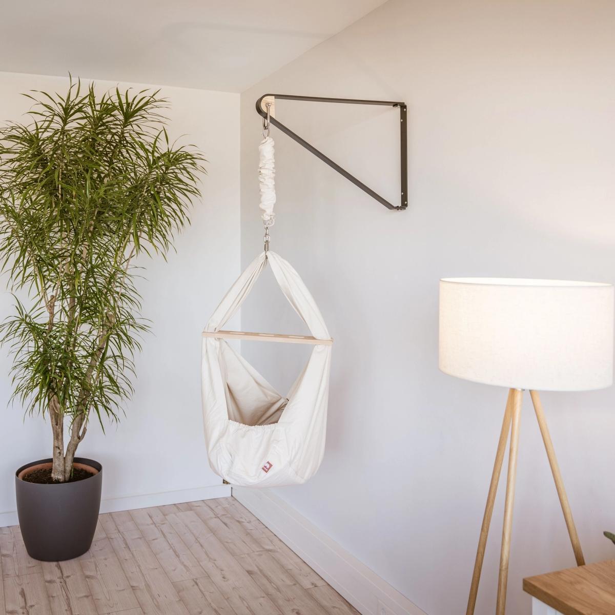 Wandhalterung für Federwiege mit Lullaby Federwiege in einem hellen Zimmer neben Pflanze und Stehlampe