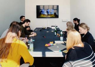 Group of people sitting at a black table in front of a screen with a clock