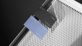 Two business cards, one blue, one black, with NLX logo embossed, laying on a white metal surface.