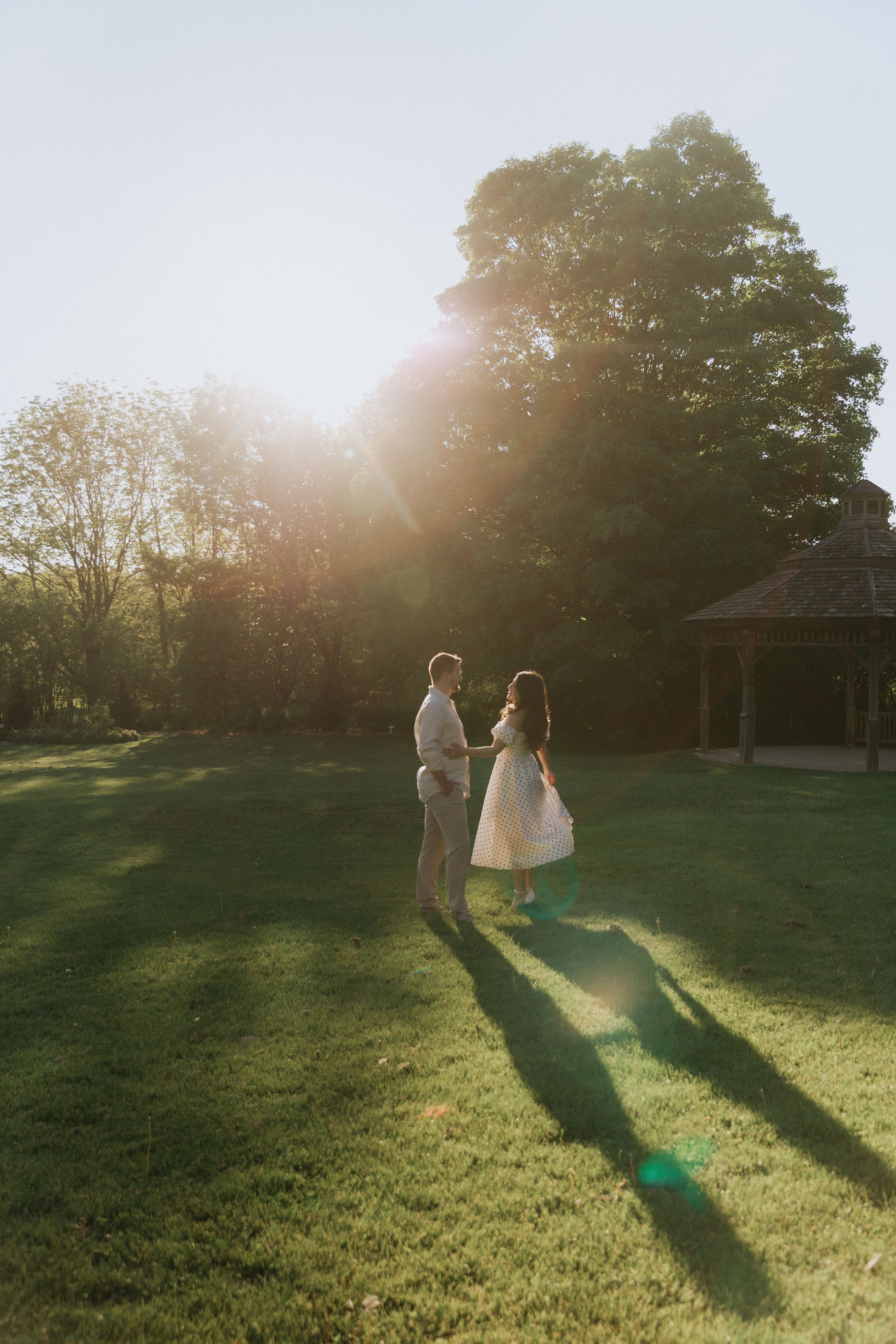 Distant couple stand beneath a tree on a broad lawn at sunset.