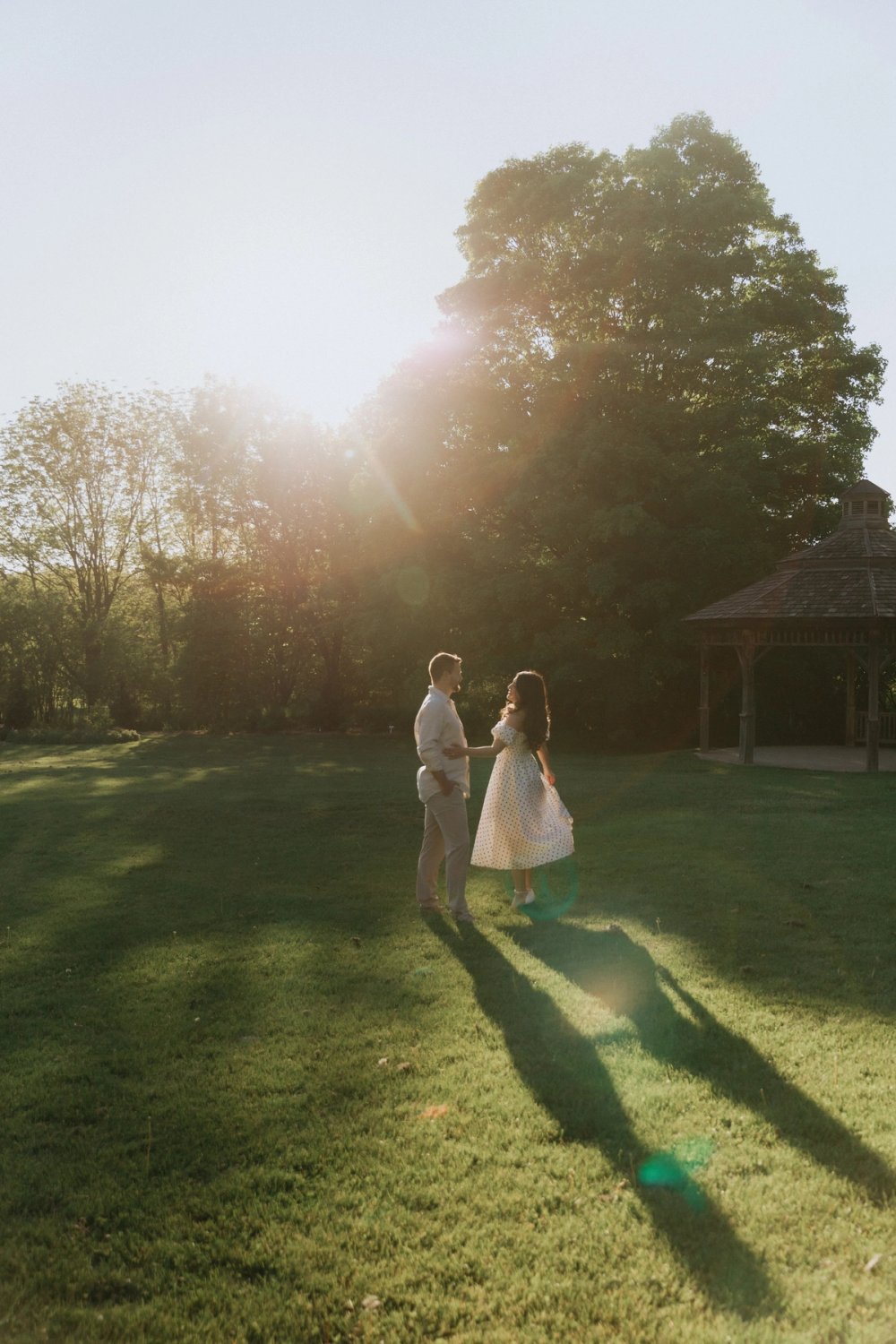 Distant couple stand beneath a tree on a broad lawn at sunset.
