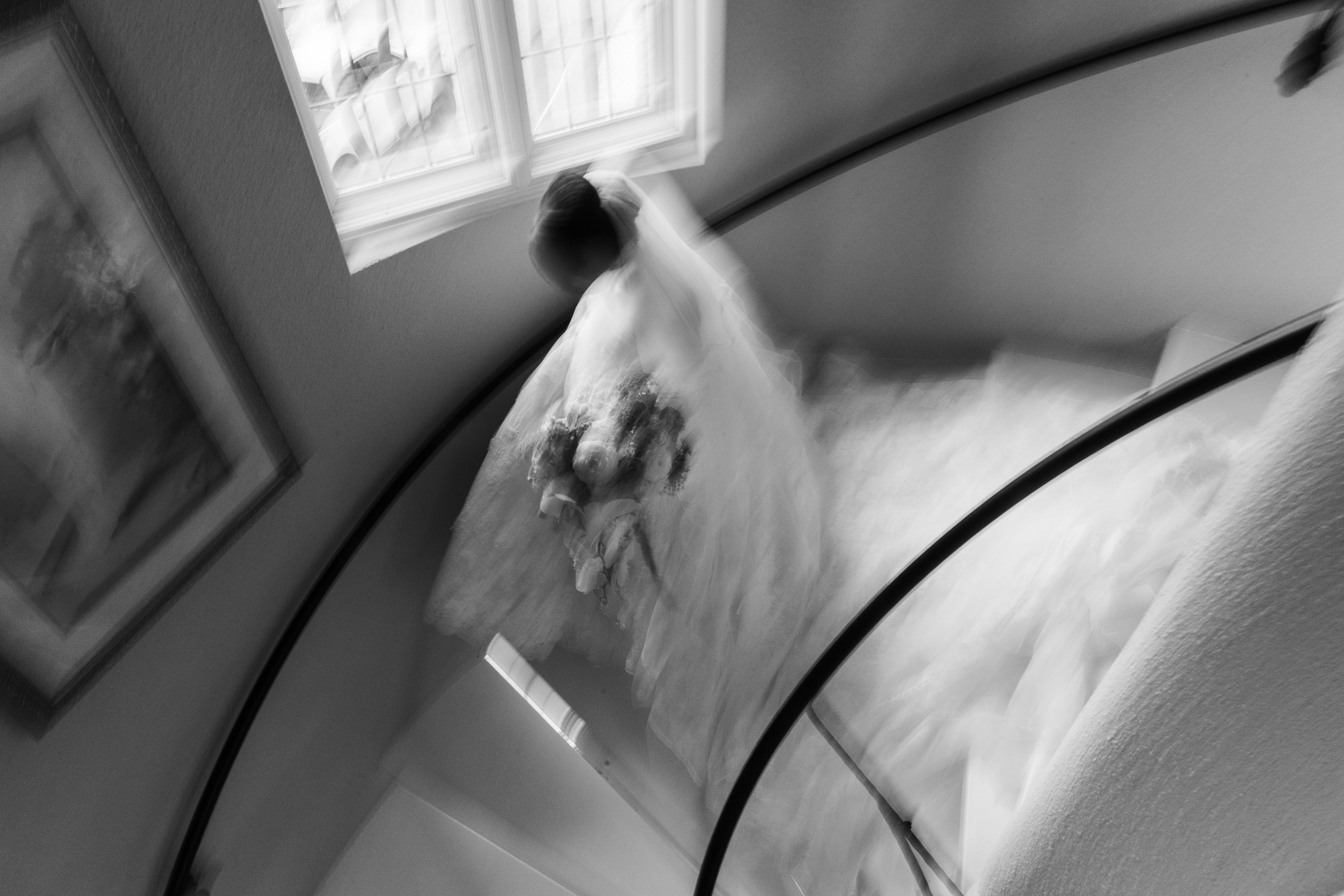 A black and white overhead photograph of a veiled bride holding a bouquet on a curved staircase at Lincoln Estates, with motion blur around her dress.