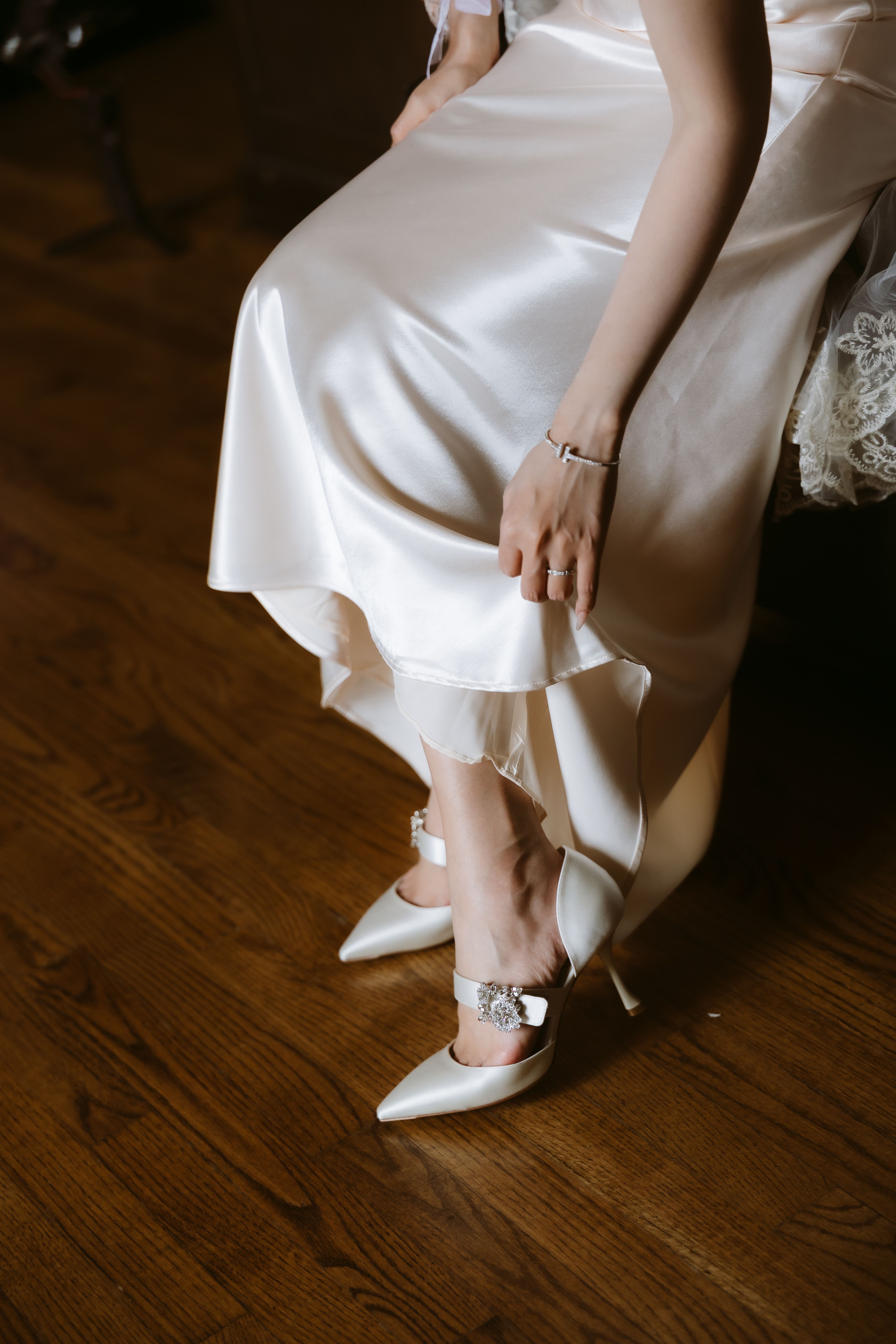Close-up of the bride's satin dress, ring and white pointed shoes with sparkling buckles on a wooden floor at Casa Loma.