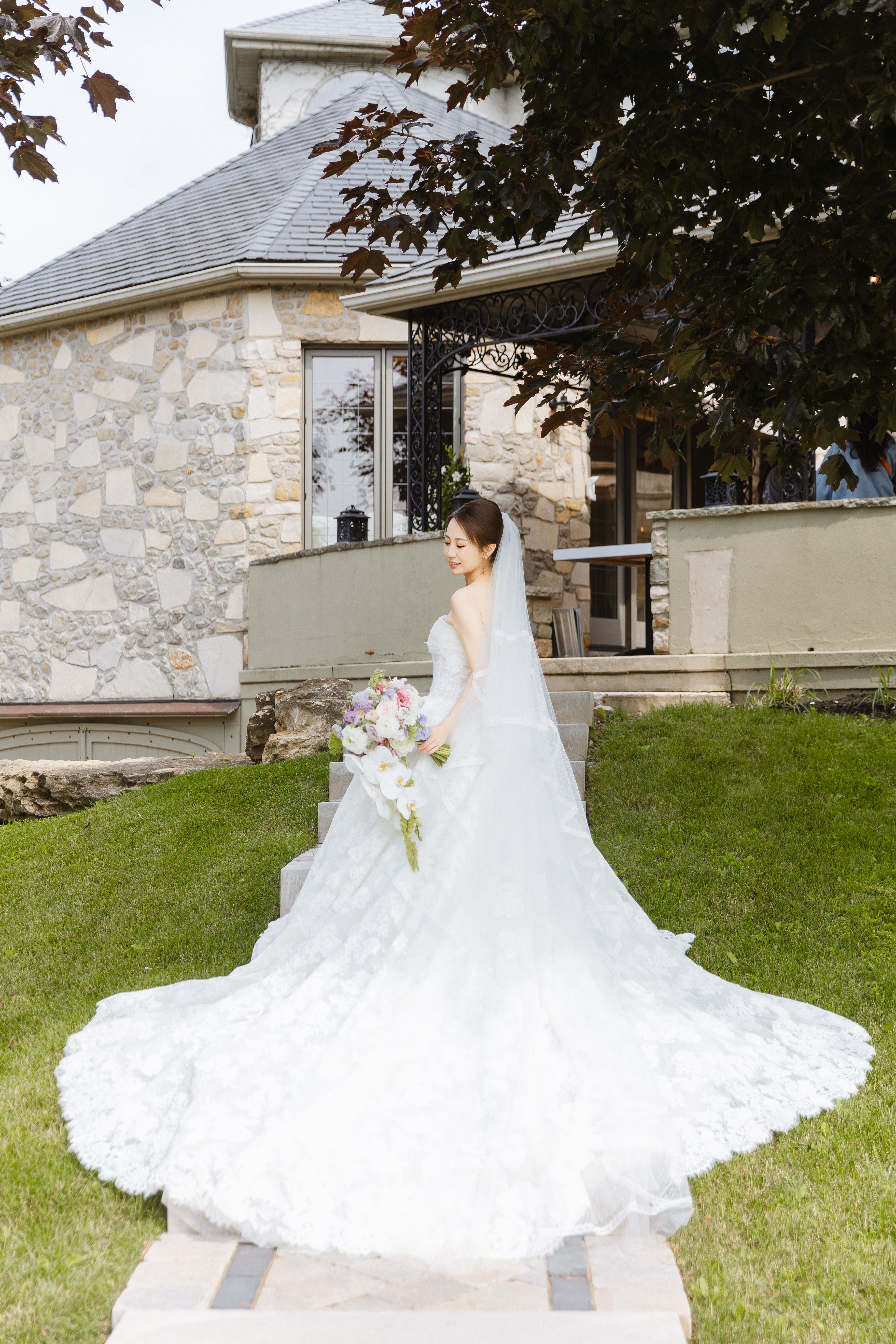 A bride holding a cascading bouquet on garden steps outside the manor at Lincoln Estates.