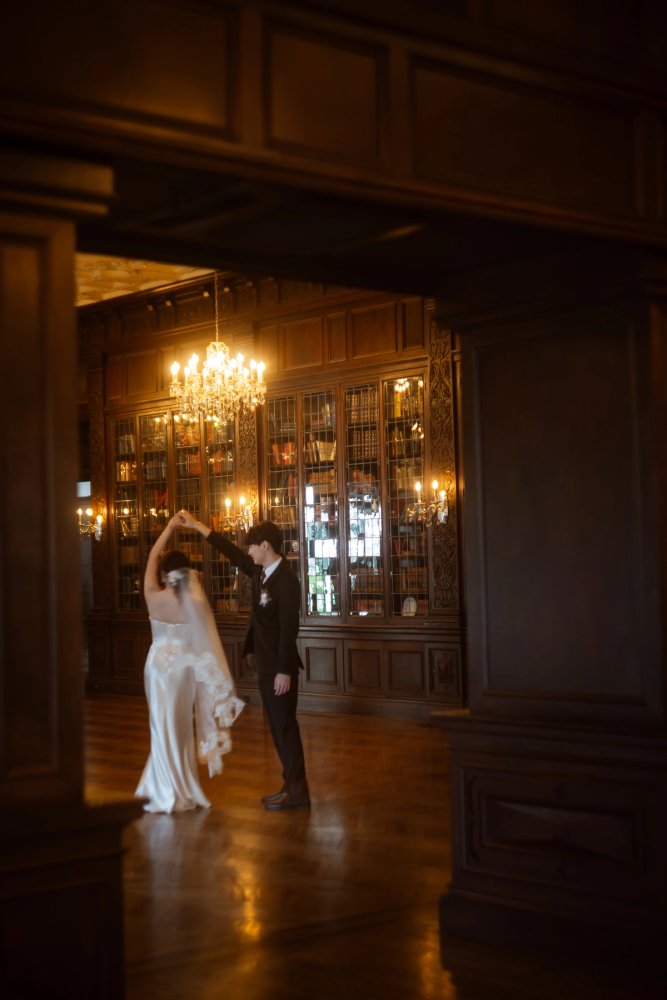 A couple turn with their hands raised beneath a chandelier in a wood-panelled room with bookcases at Casa Loma.