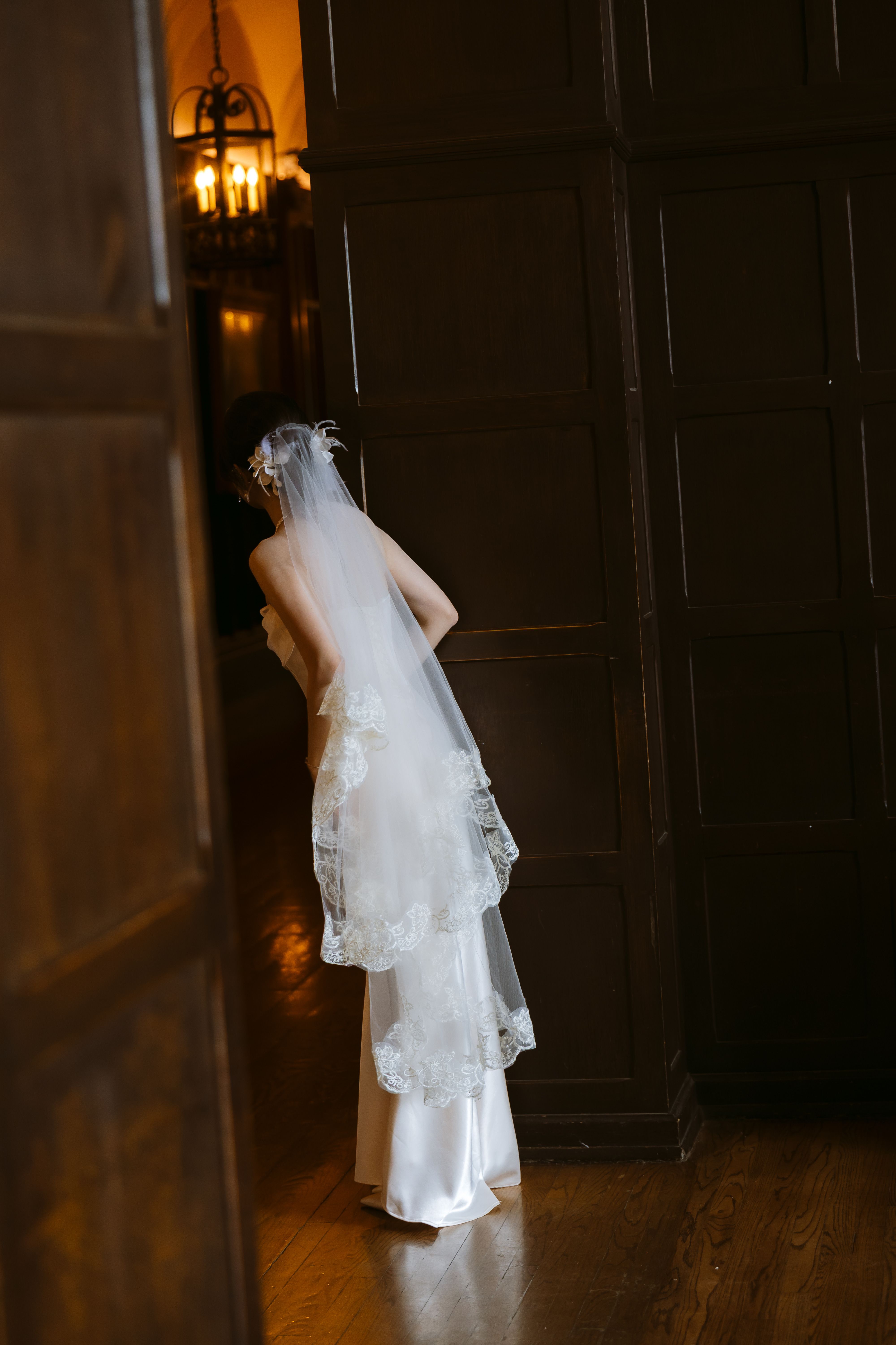 Bride seen from behind beside a dark wooden doorway at Casa Loma, wearing a long white veil with lace edging.