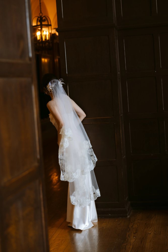 Bride seen from behind beside a dark wooden doorway at Casa Loma, wearing a long white veil with lace edging.